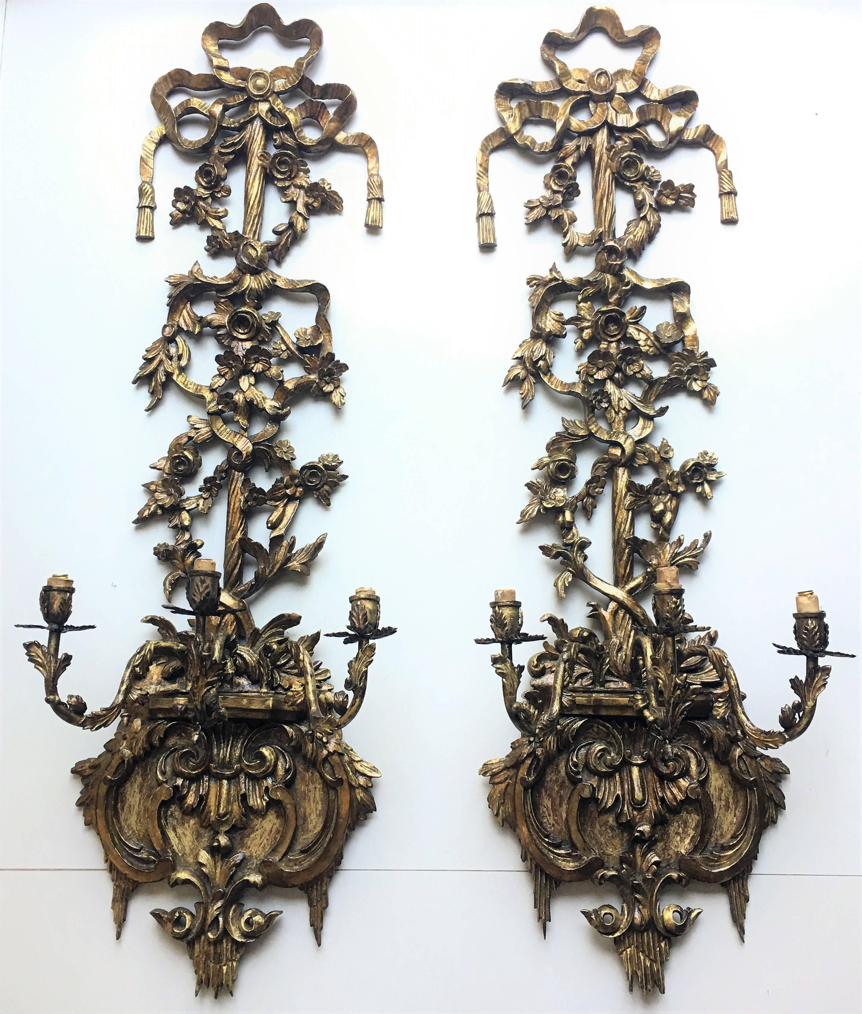 This monumental pair of three-light sconces is hand-carved gilded gold. The delicate ribbon winds upward from the candle cups and ties the bundle of wheat sheaves, ending in a crowning bow. The carvings are superbly detailed, and reminds one of the
