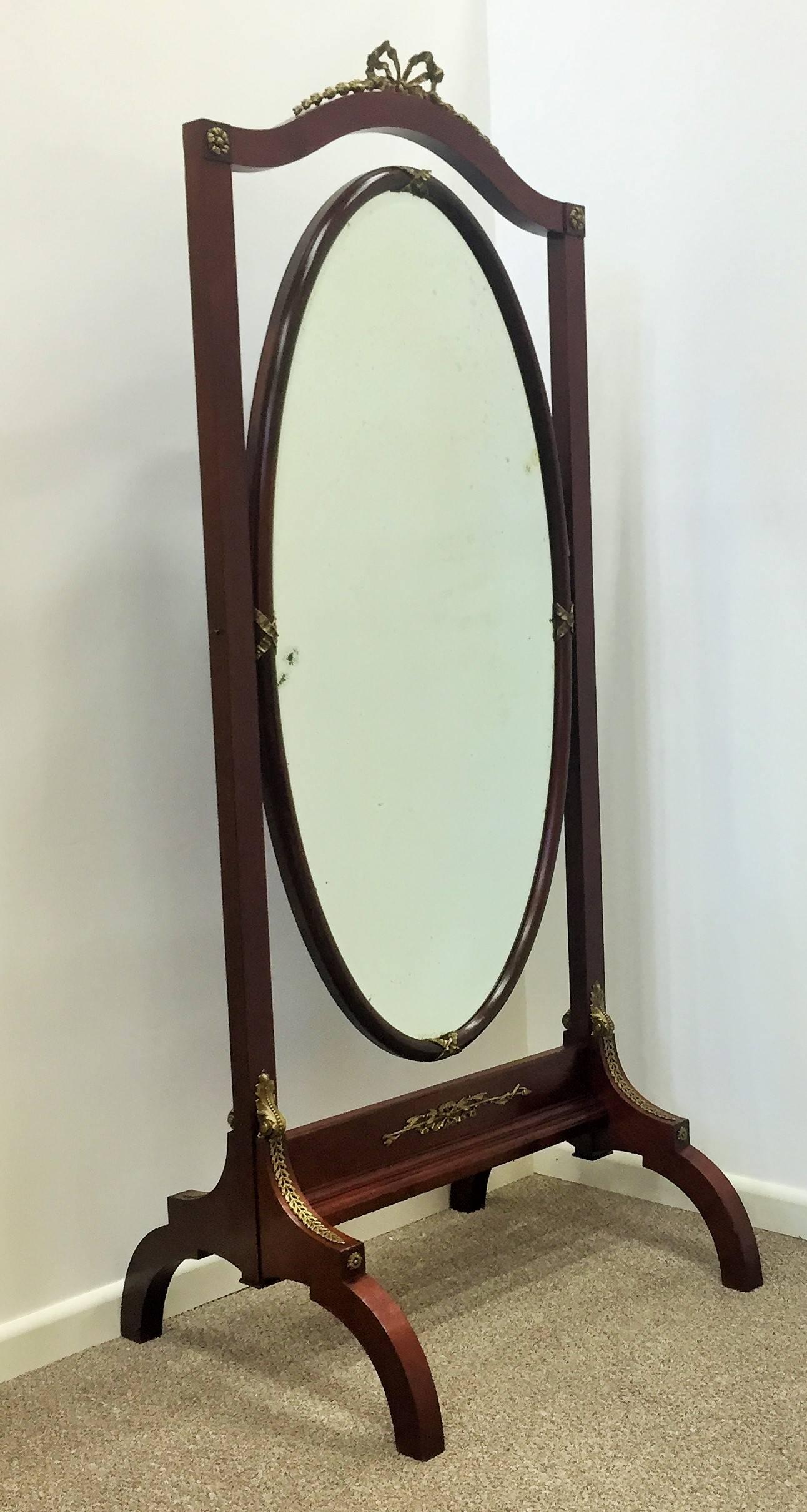 Empire period cheval mirror. Mahogany and mahogany veneer over oak. The arch topped frame holding the mirror supported on two columns, surmounted with finely incised gilt bronze urns, and with finely incised gilt bronze rings at the base of the