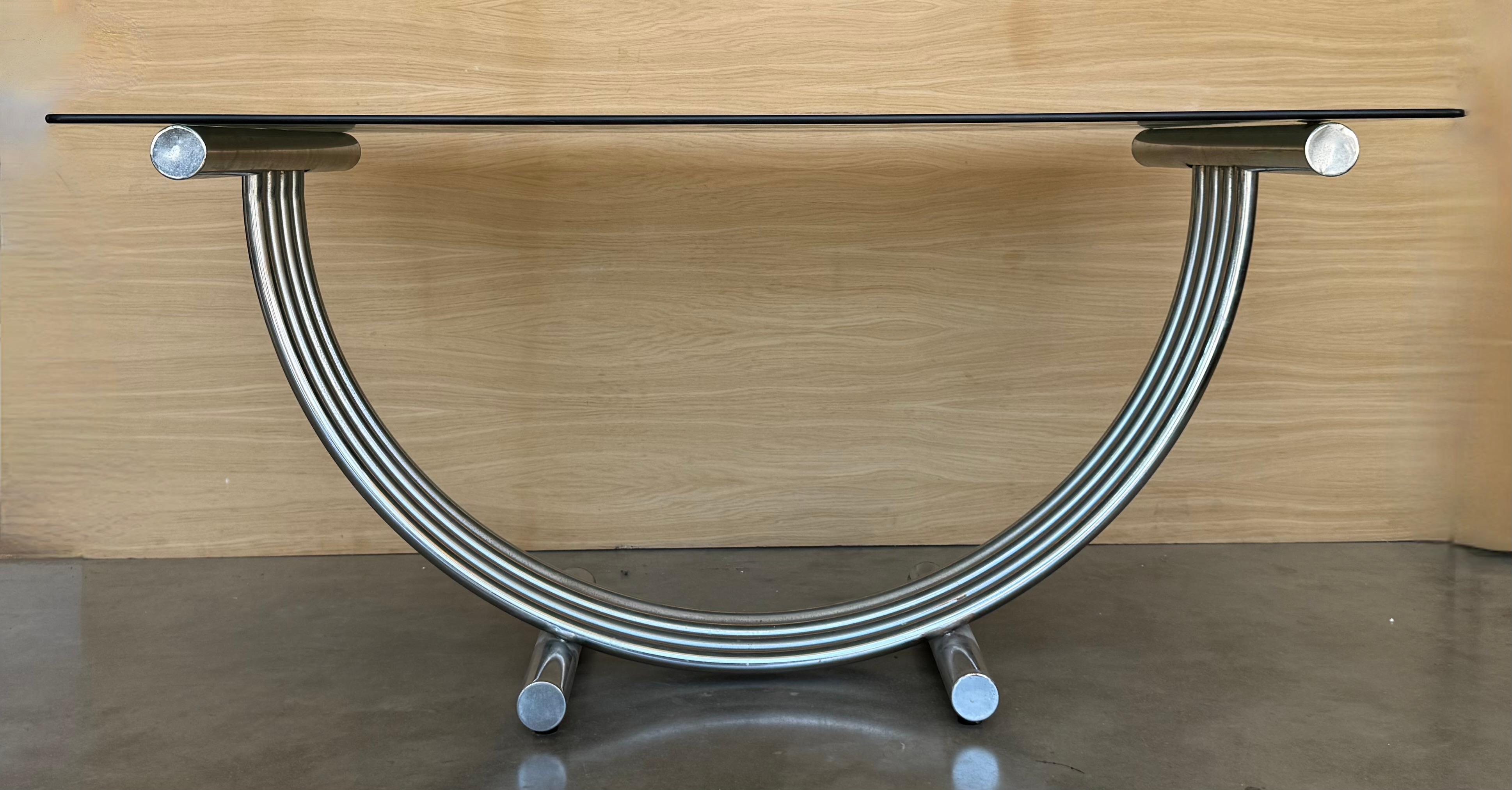 Table de salle à manger sculpturale de style Art déco dans le style Romeo. La base tubulaire à arc incurvé présente un design rayé en laiton et en chrome avec un plateau en verre fumé. Un superbe bureau surdimensionné ou une table console.