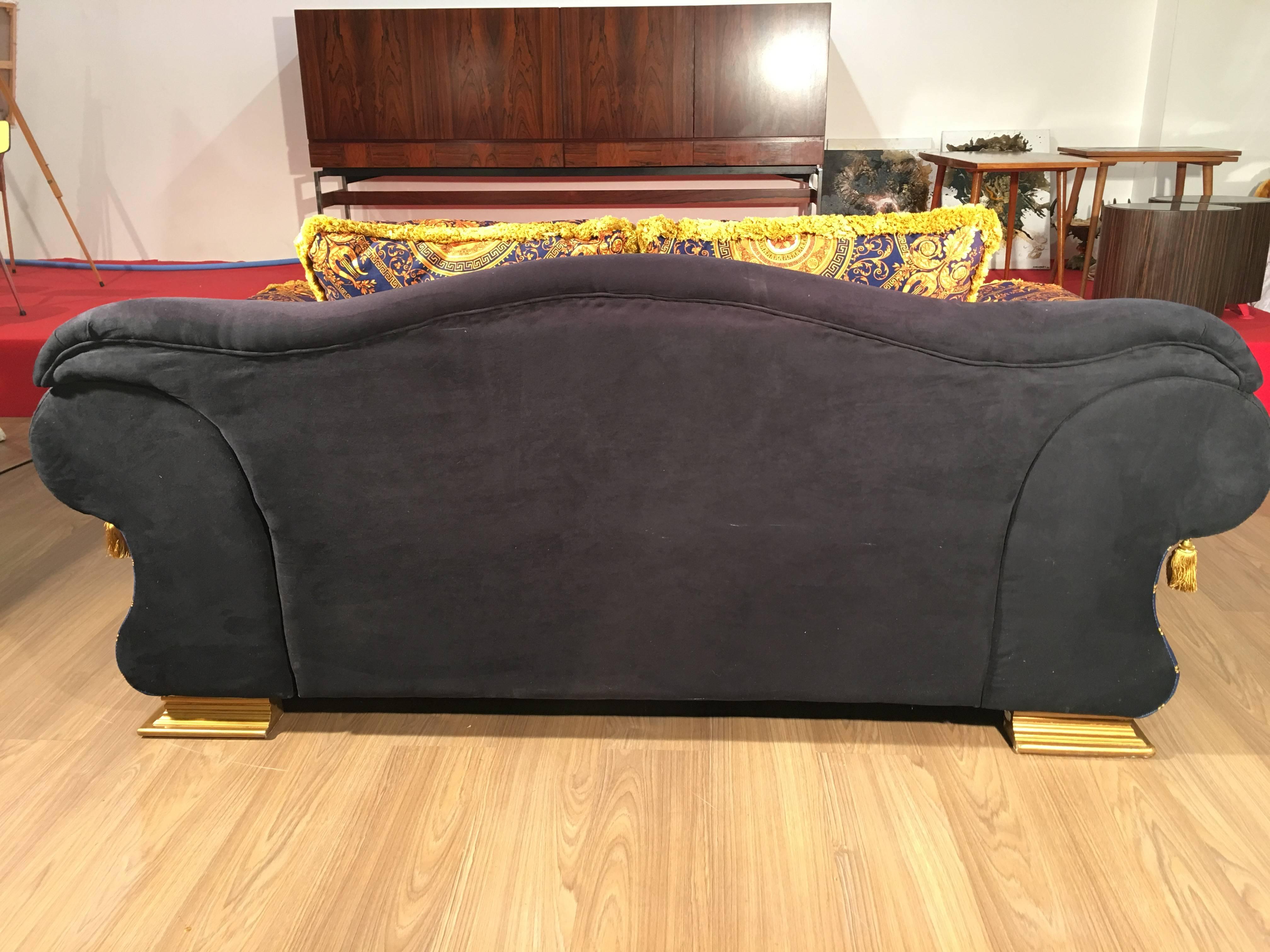 This amazing night blue velvet couch in Versace style is enhanced with a royal blue and gold quilted facing, gilded medallions and decorations in round bump. It is adorned with bronze and gold velvet and silk cushions richly decorated in antique.