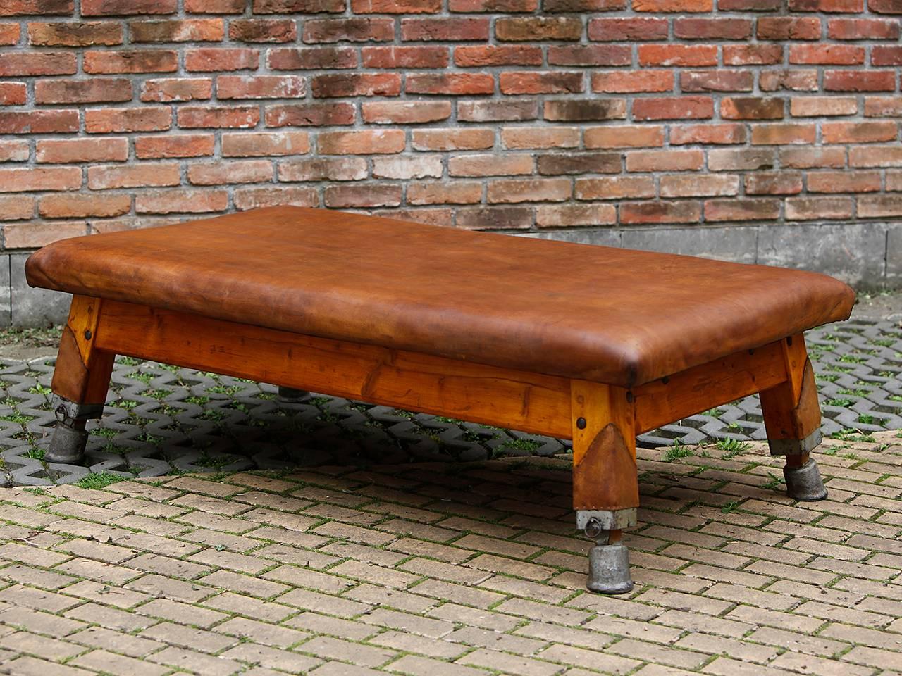 This vintage gymnastics tournament table is from a Czech school sports hall. It was cut to a height of 55 cm and has leather-covered legs and a removable panel. The leather was cleaned and preserved and the wooden parts were restored. The thick cow
