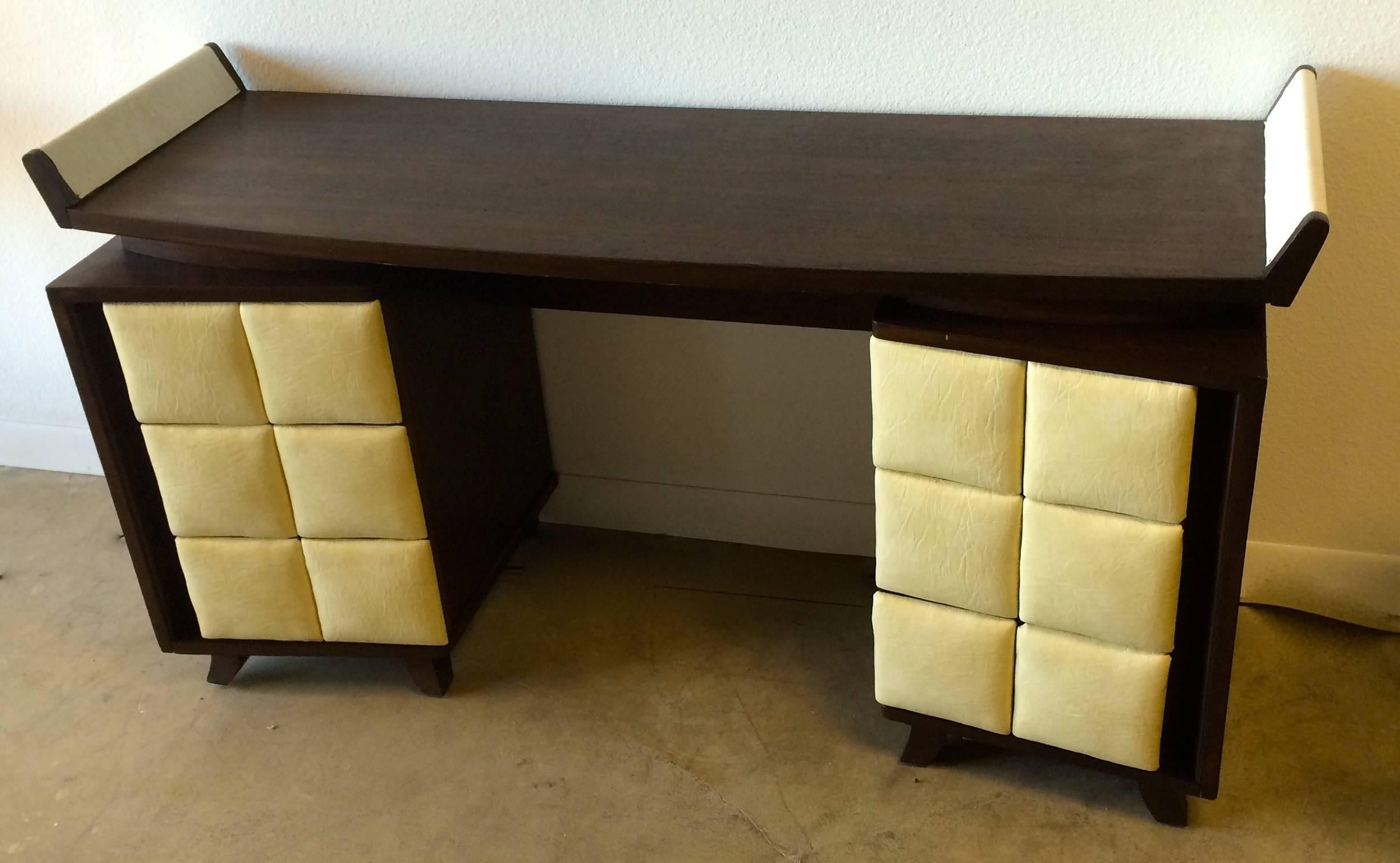 This desk designed by Gilbert Rohde was part of a series of Rohde-designed case goods released by Herman Miller in 1941. Original cream leatherette on all six drawers and each side wing. The highly sculptural quality of the Mahogany case marries the