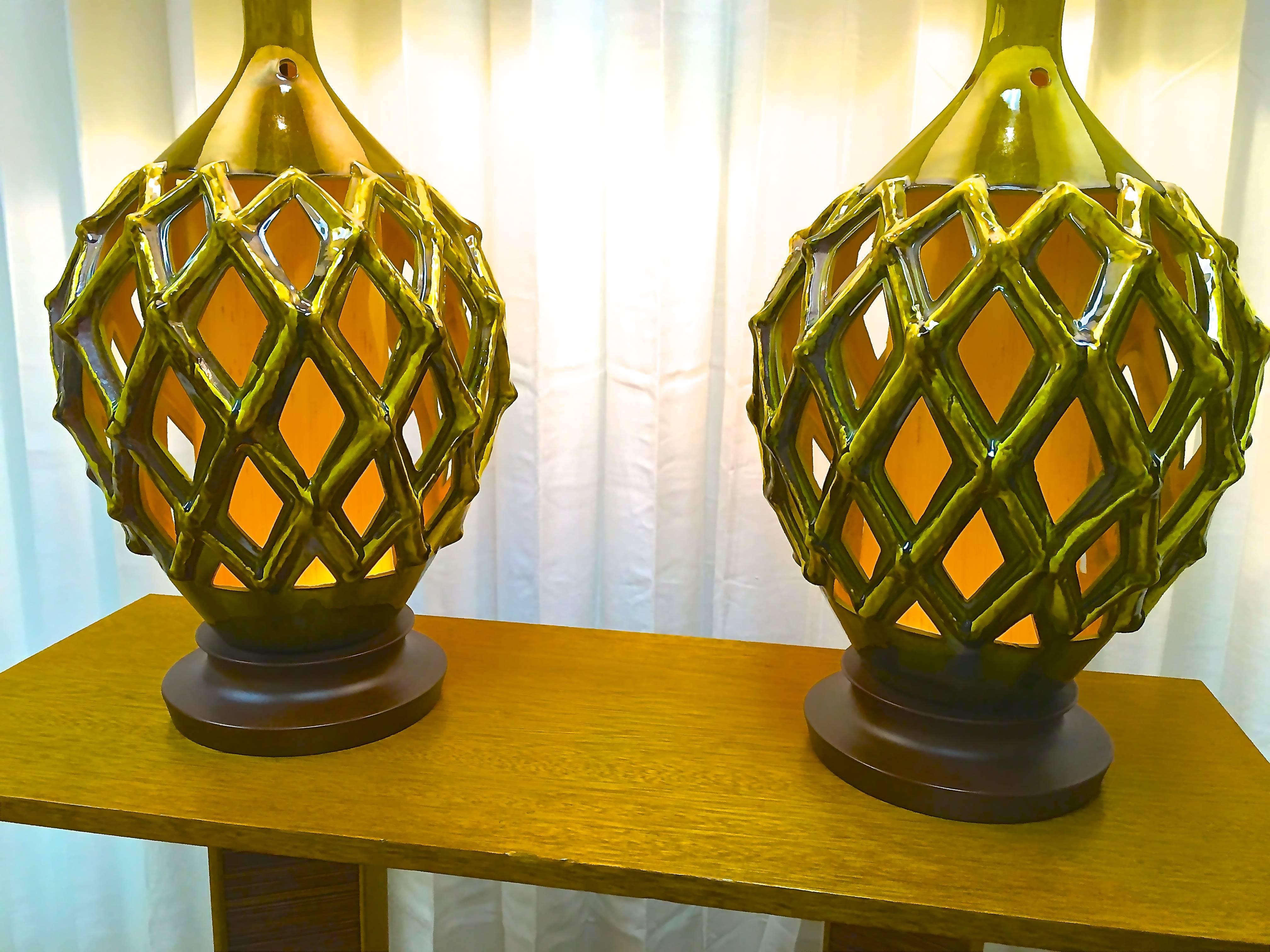 The pair of lamps glow from within on a separate switch through the open lattice design. They have bronze-colored metal bases and a variety of green to gold hues. Lamps are completely rewired with brand new shades.