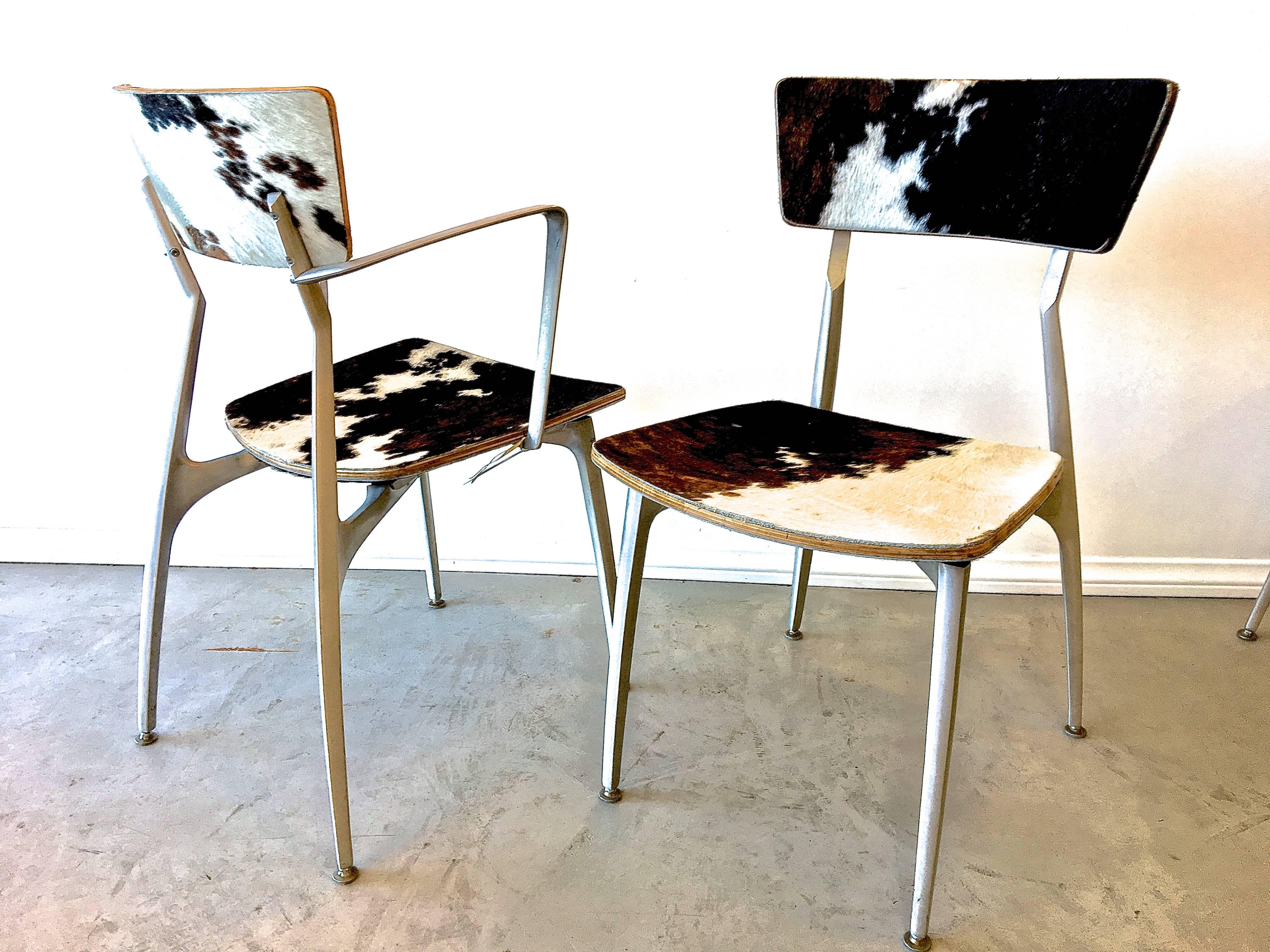 Mid-Century Modern set of four dining height chairs - two arm and two side - sculpturally formed from sand-cast aluminum and covered in handsome cowhide. The angles and minimal lines of each chair provide ergonomical comfort as well as a striking