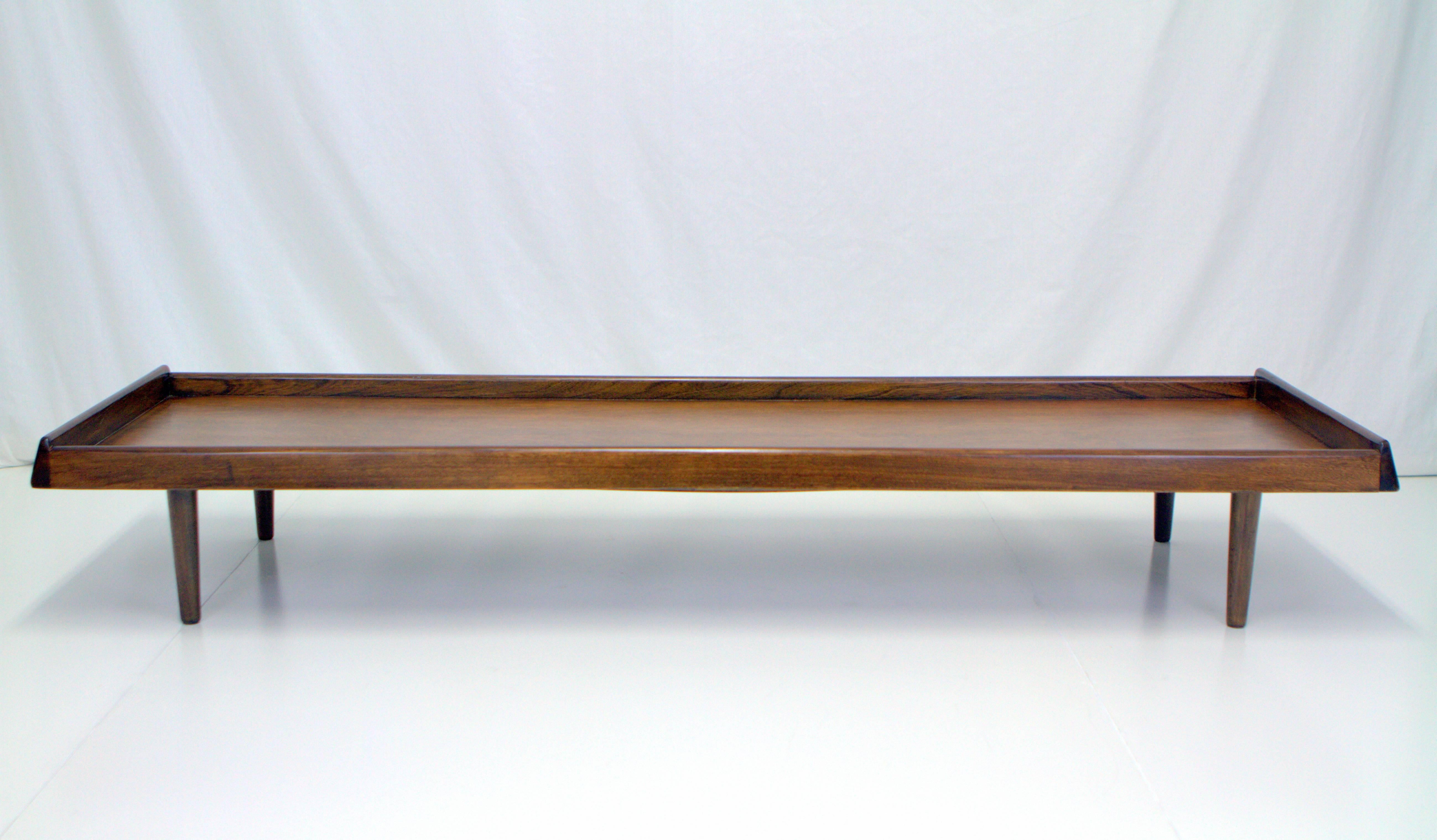 Mid-Century walnut cocktail table or bench. Very long and low with tapered sculptural sides and a recessed surface. Can be a bench or daybed with upholstered cushion. Solid construction with under mount support and screw on tapered legs.