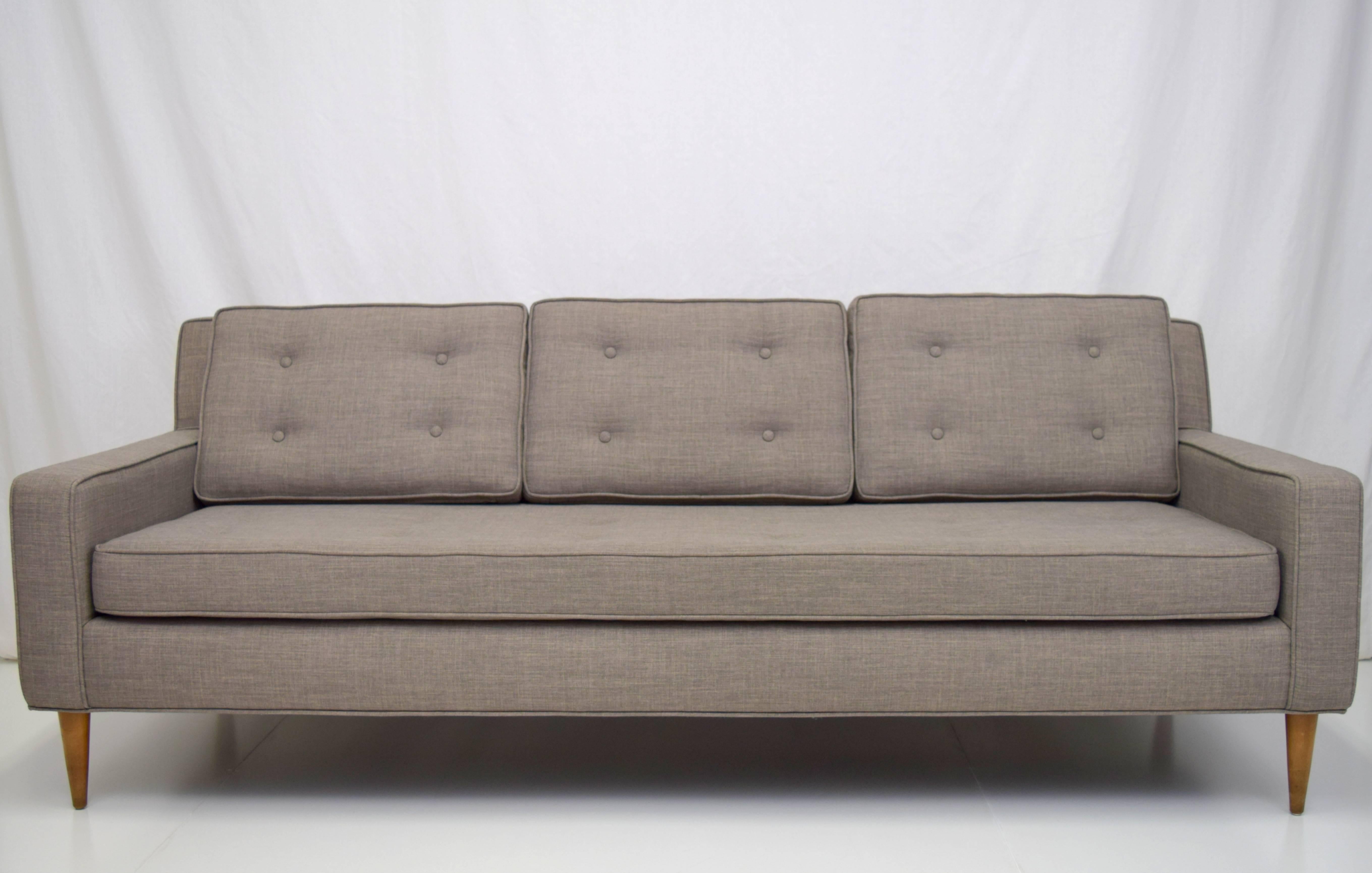 Perfectly scaled and proportioned button tufted sofa in the manner of Paul McCobb. Three back cushions over bench seat with conical legs. Upholstered in silver blue textured linen like fabric.