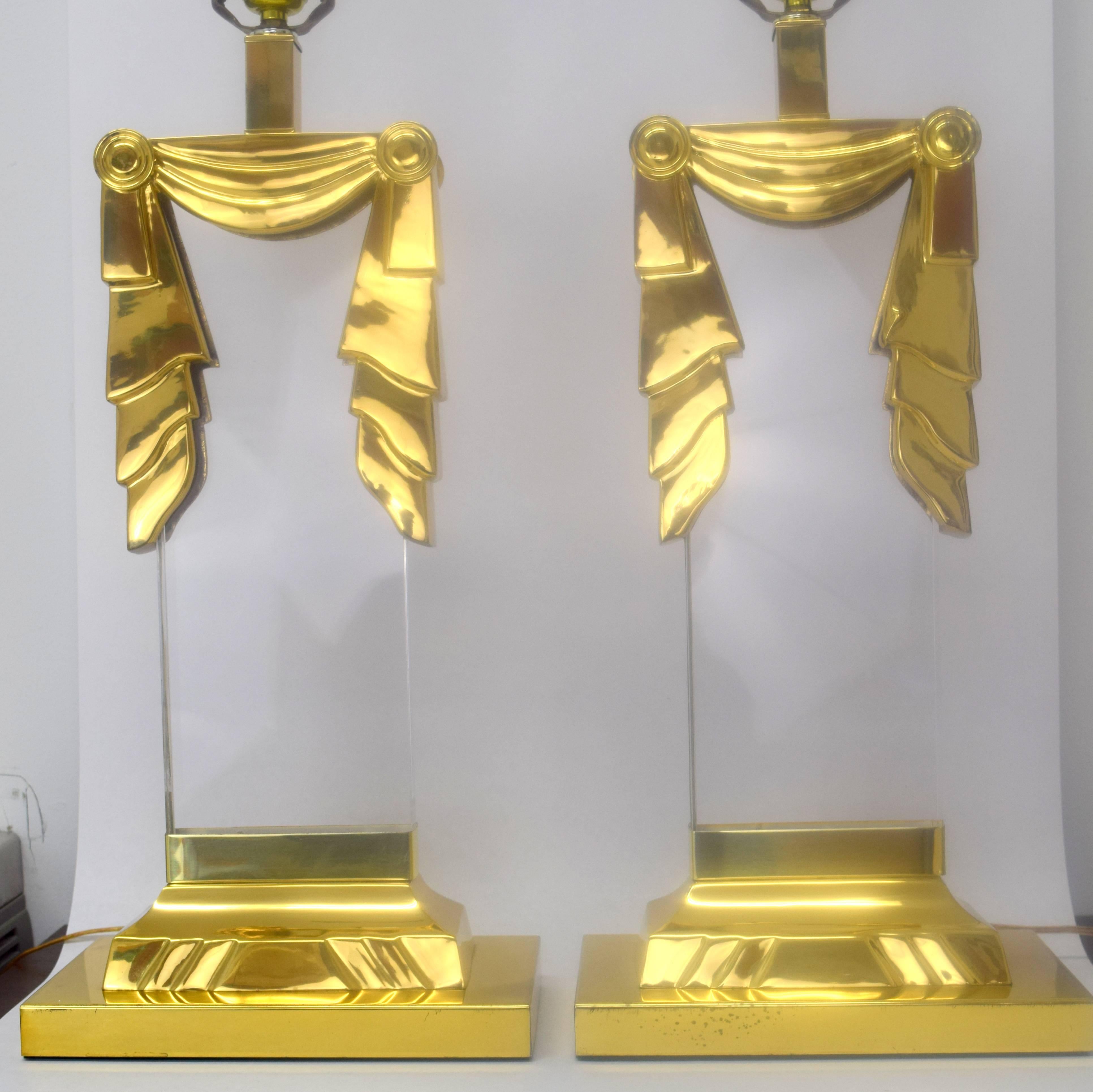 Fantastic pair of lucite and brass lamps in square column style with swag motif. Polished brass with minor patina and wear, lucite clear and free. Electrical cord enters base then travels up side inset in lucite. Shown with vintage shades, not
