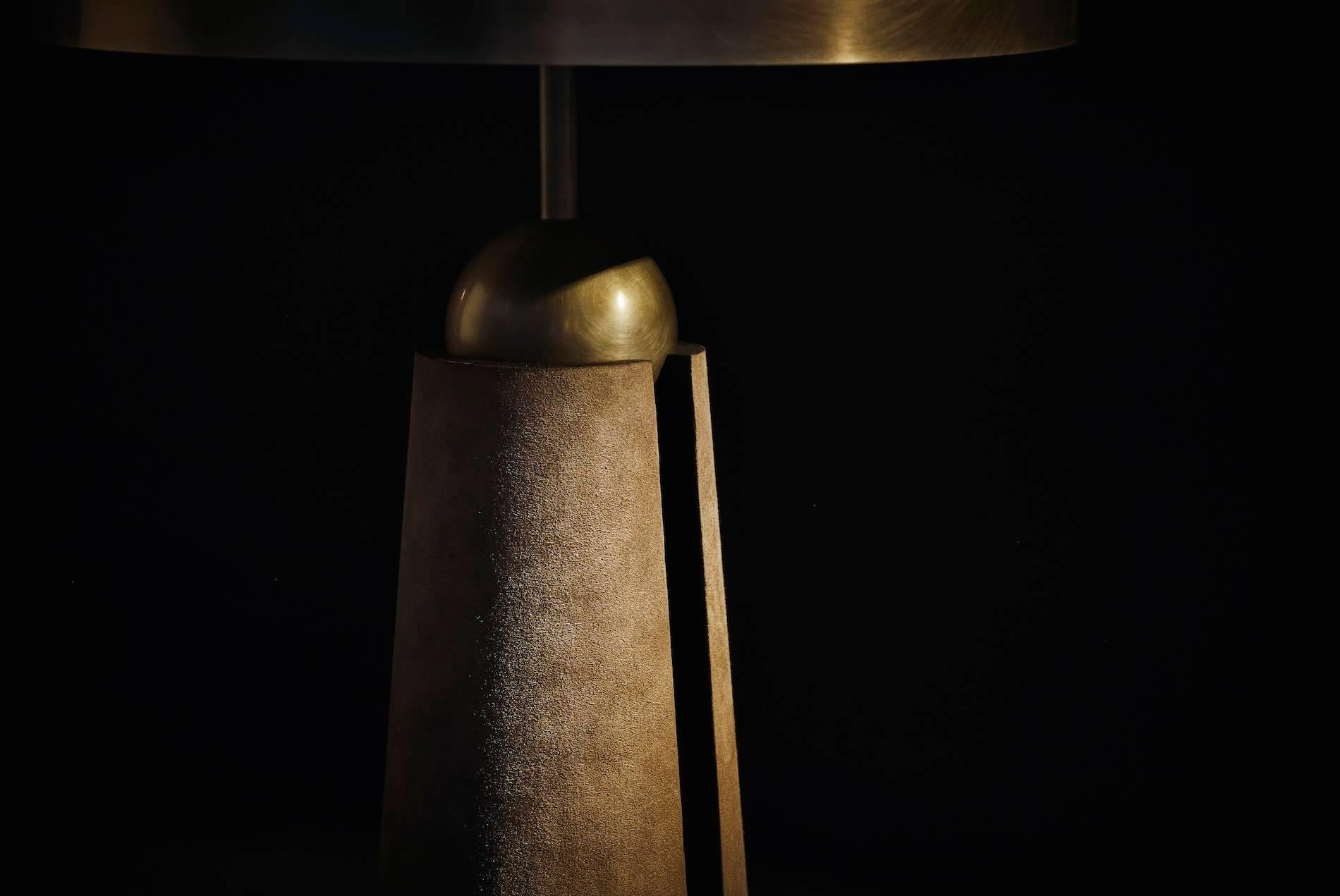 The Metronome series evokes the measure and balance of its namesake. A patinated brass sphere perches atop the conical base, which is hand wrapped in calf suede to provide a lush tactile contrast. A channel in the firmly grounded base reveals an