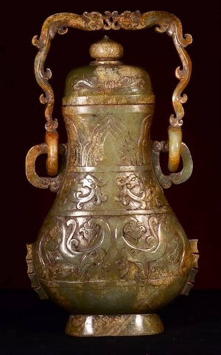 Chinese nephrite jade archaistic covered vase, Qing dynasty.

Carved to resemble an archaic bronze covered Hu (ritual wine vessel) with dragon handle attached by loose rings, the surfaces utilizing areas of the stone's natural skin and color