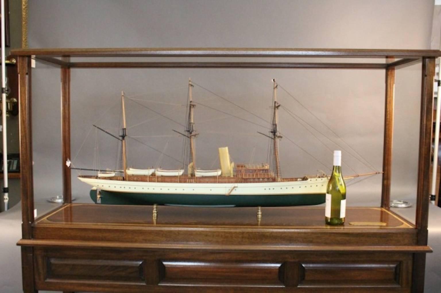 Cased model of the steam yacht “Aphrodite”. “Aphrodite” was launched in Bath, Maine in 1898, designed by Charles Hanscom. The long trunk cabin carries six lifeboats and launches. Rigged with three masts, the two foremasts are square rigged. Brass