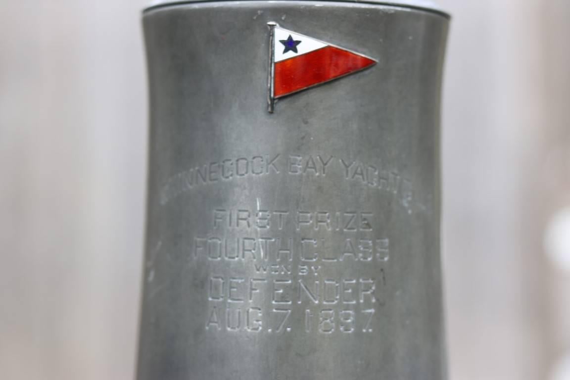 Shinnecock Bay Yacht Club trophy cup engraved "First Prize, Fourth Class - won by Defender, Aug. 7, 1897". Has yacht club burgee in cloisonné. Clear glass bottom. Dimensions: 8" H.