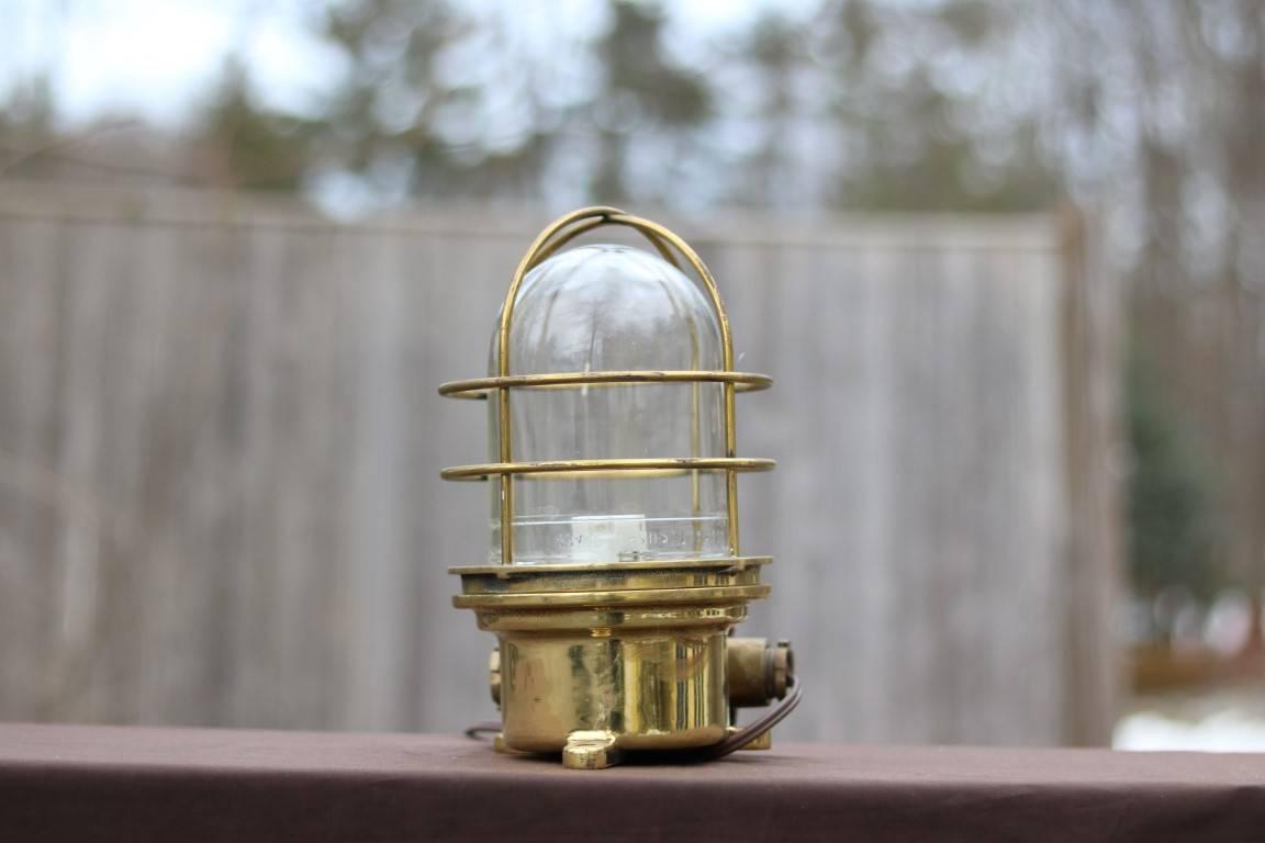 Heavy brass bulkhead light with glass globe, and protective cage. Electrified. Dimensions: 11" H x 7" diameter.