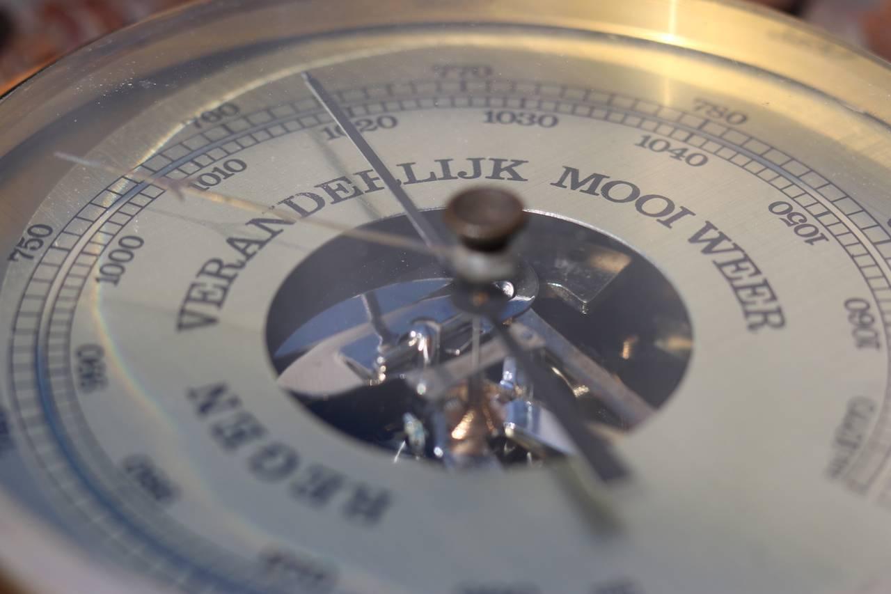 Aneroid barometer with polished brass face on an ornately carved two-toned backboard with hanging loop. Marked "West Germany". 10" overall, diameter. 5" face diameter.