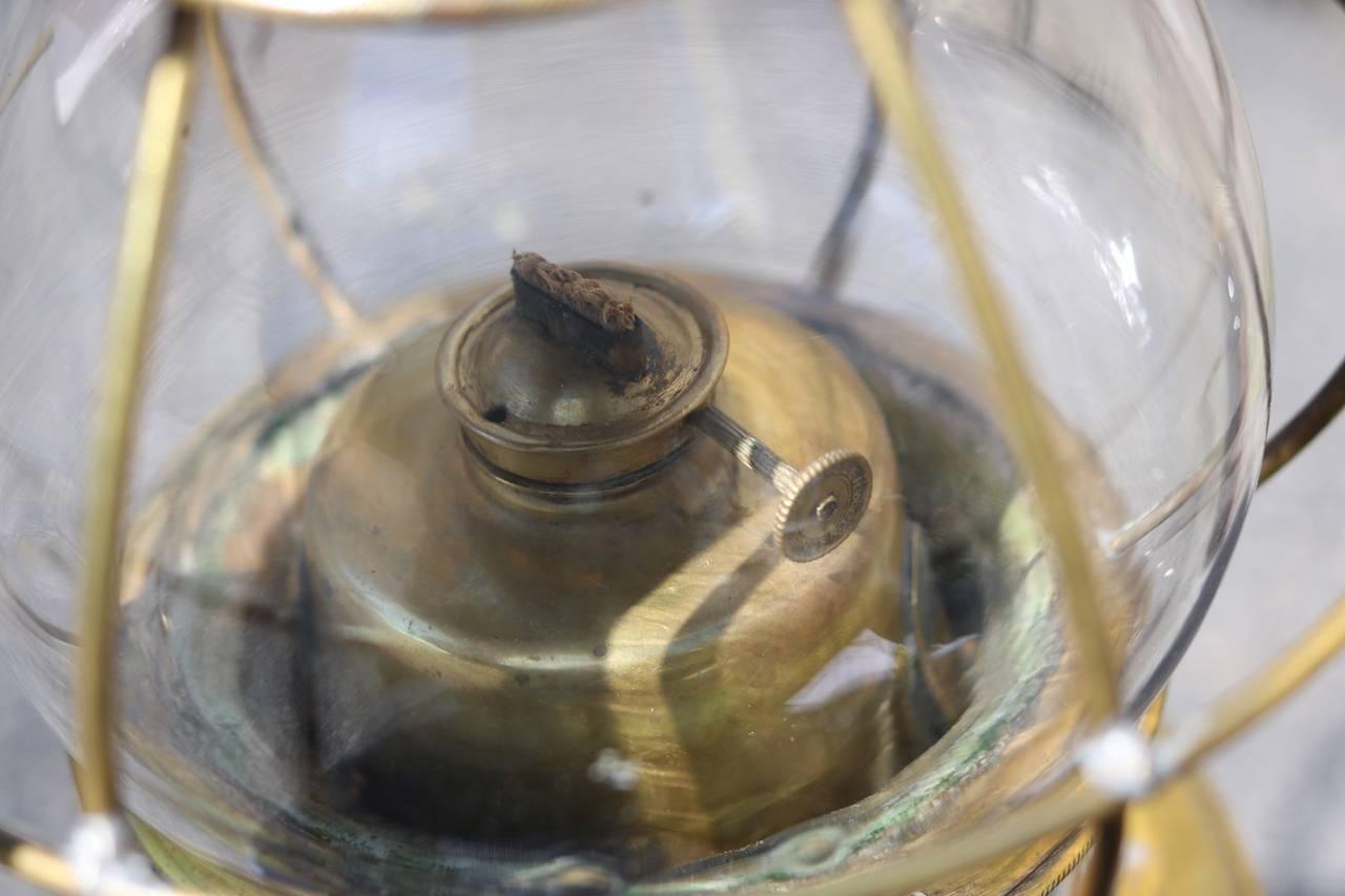 Early brass cabin lantern with glass globe, vented top and bottom, protective bars, carry handle and oil burner. Measures: 16 1/2" tall with handle.