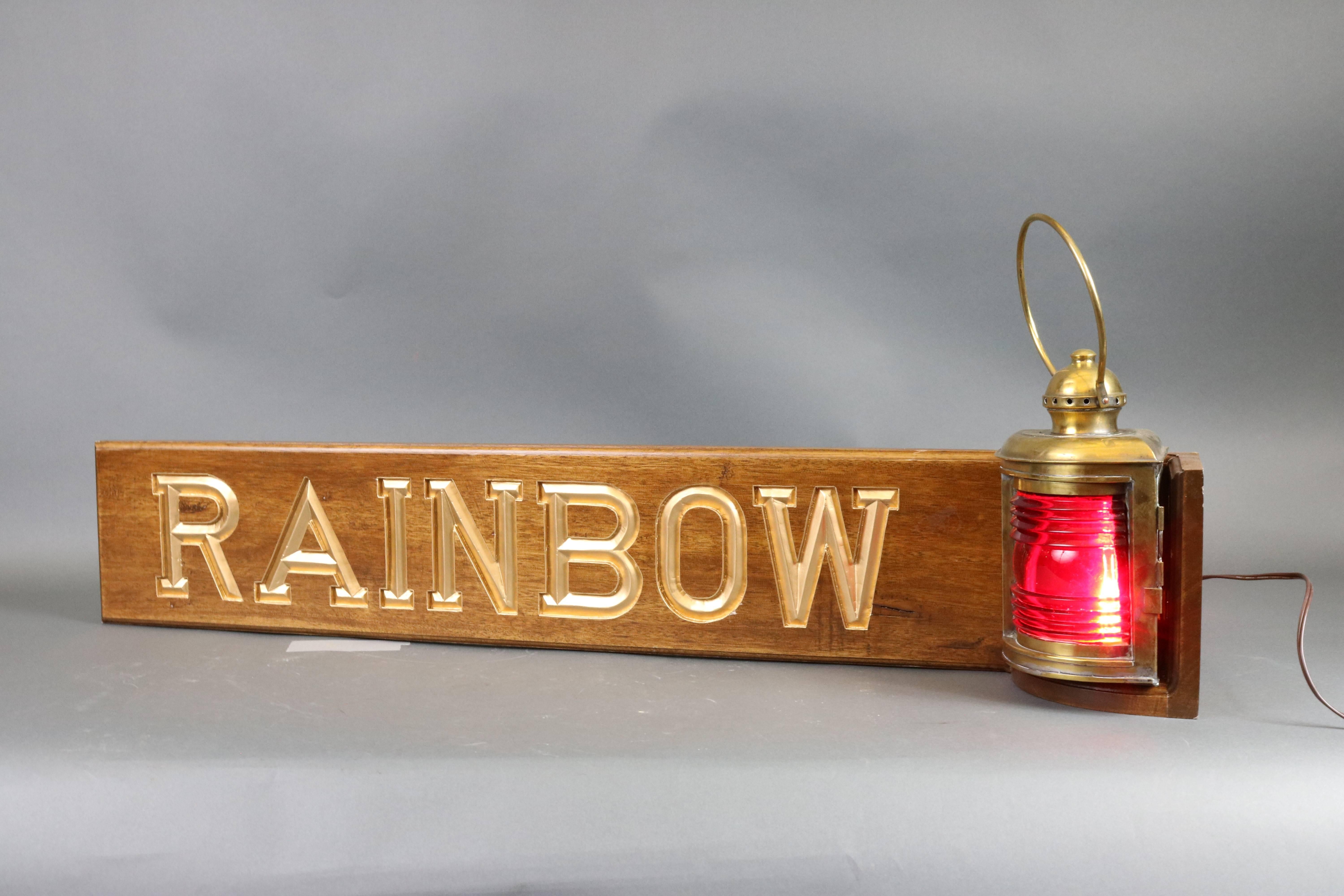 Deeply carved mahogany name board with "Rainbow" in gold paint and fitted with a solid brass antique ship's lantern. Electrified. Dimensions" 42" L x 6" W x 11" H (w/o handle).