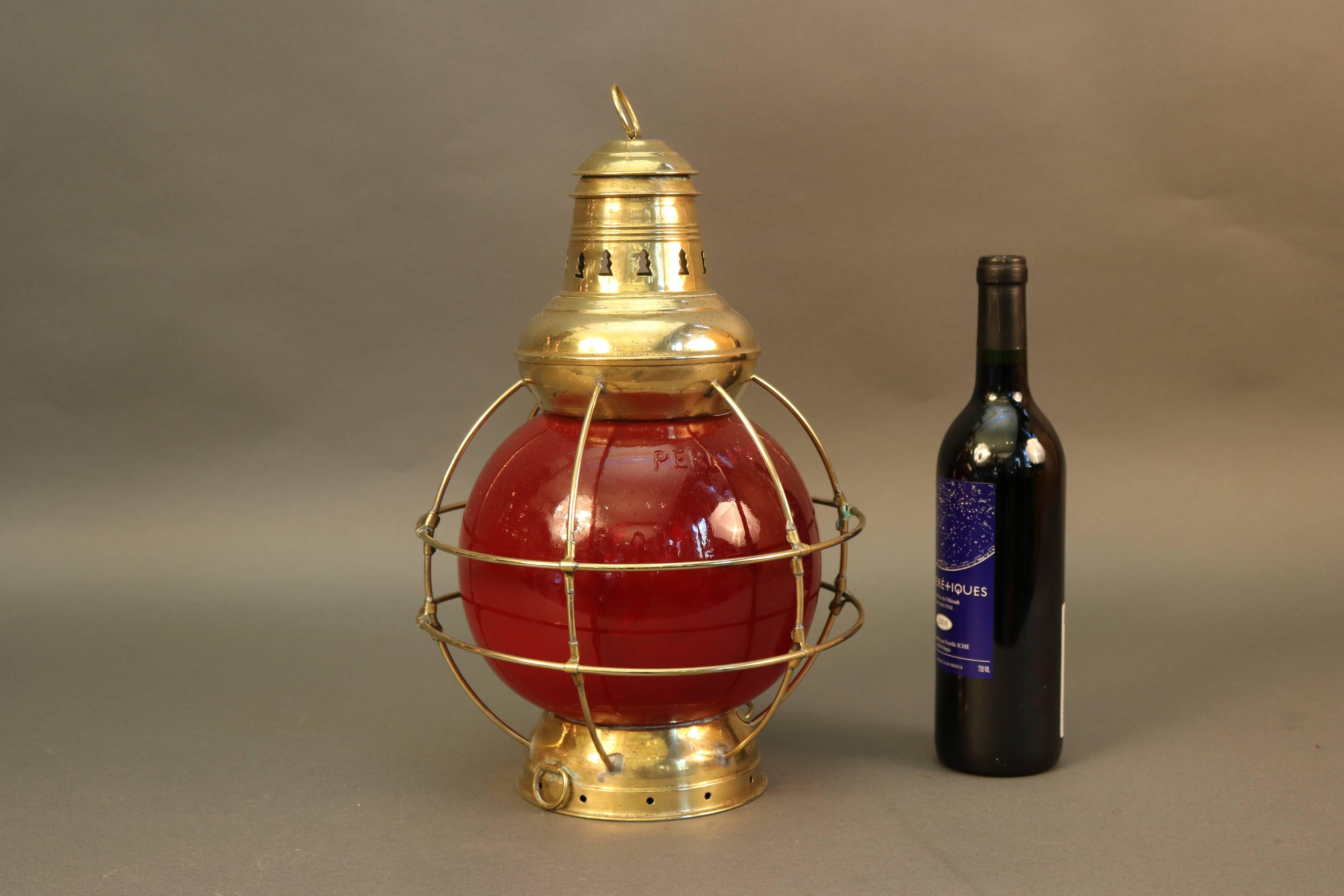Solid brass Perkins Marine ship's lantern with rich red lens and protective brass bars, vented top with hoisting ring. Dimensions: 10" L x 10" W x 14" H.