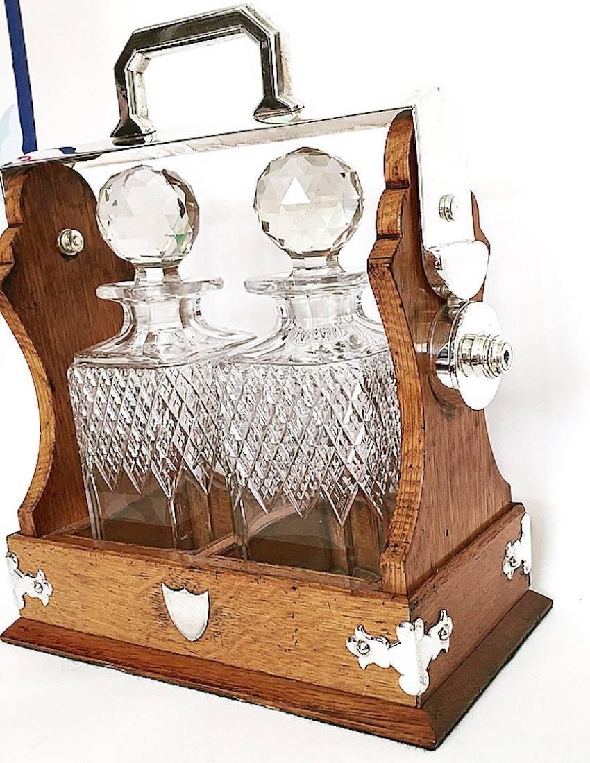 English oak tantalus with two crystal decanters and original key. Silver plated shield on front and detailed side mounts, circa 1900.