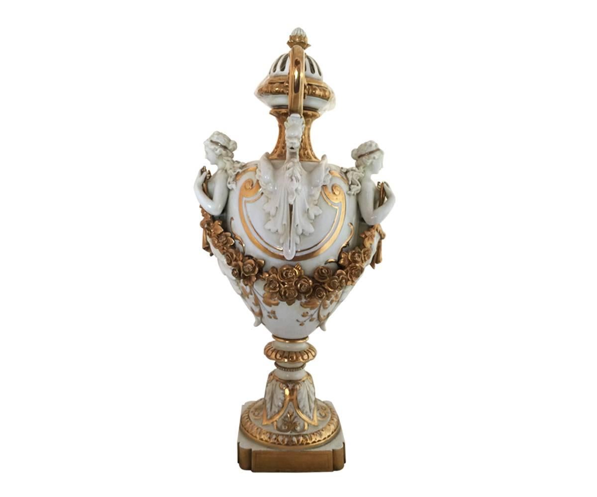 This striking pair of 19th century Capodimonte urns will be the centerpiece of any room with the well preserved gilt finish on top of a gorgeous ivory fine porcelain. The two handled urns feature a winged griffin below each gilt handle and above the
