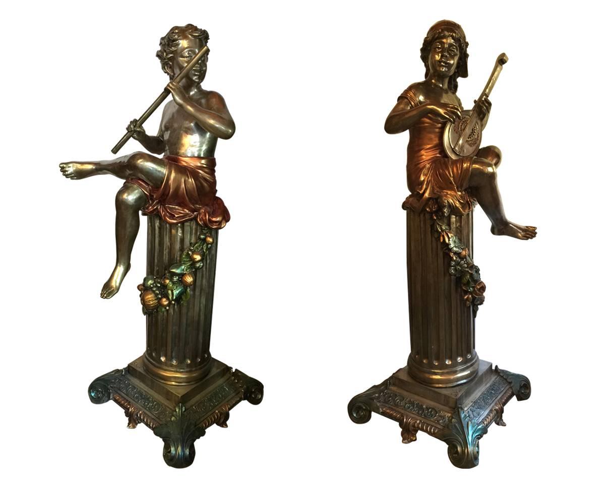 This pair of silvered bronze sculptures features two children playing music together as they glance at each other. The young boy is playing a flute and the young girl is strumming a mandolin. Integral to the piece is a fluted pedestal with a well