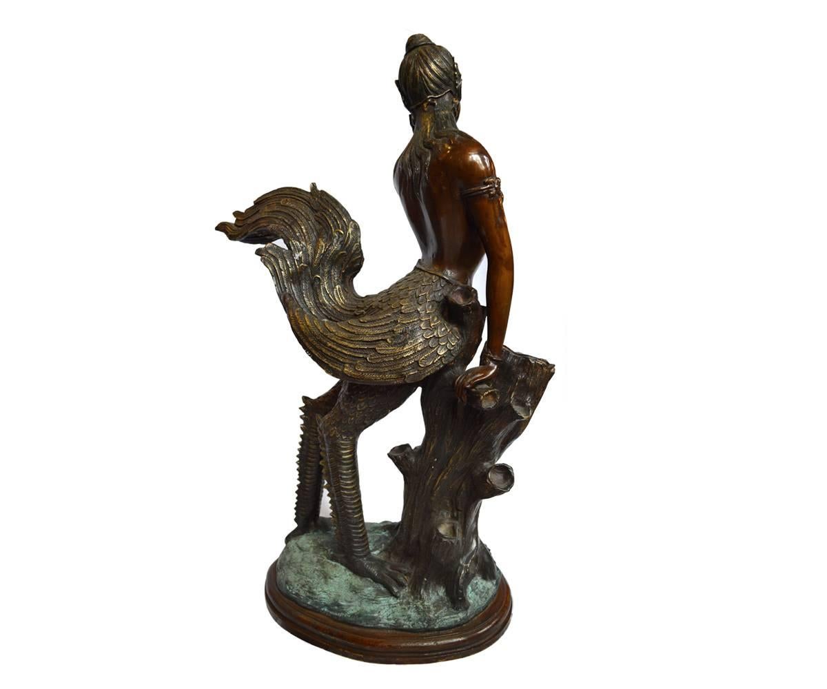 This unusual Thai bronze features a mesmerizing kinnara, a mythical creature with a nude female torso sprouting wings and unearthly legs. She is quite captivating as she poses with one hand on a tree stump and the other on her chin and cheek while