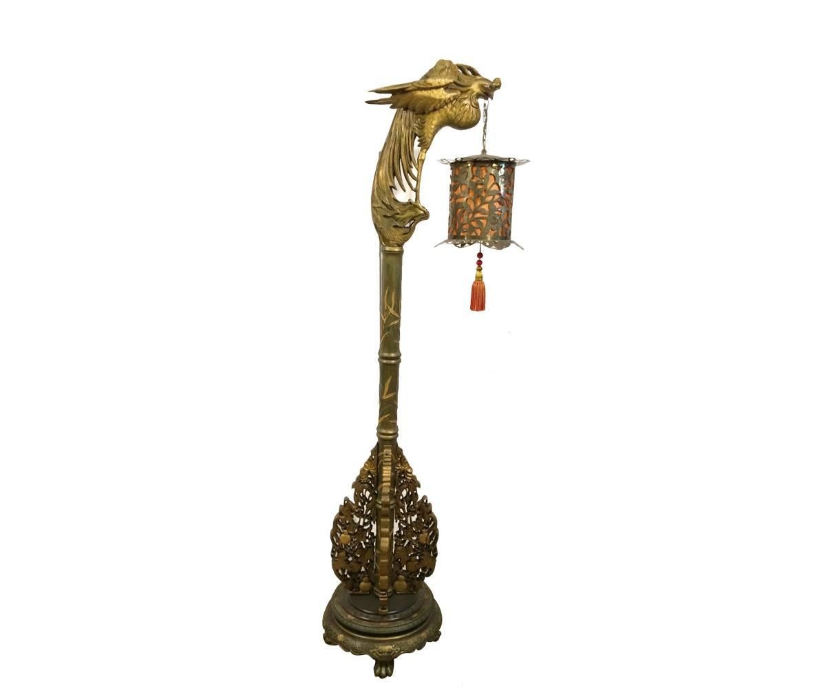 This intricately and well carved Chinese gold gilded floor lamp features a Phoenix holding a brass lantern with a hanging tassel. The carvings at the both the top and bottom of the lamp are very well done.