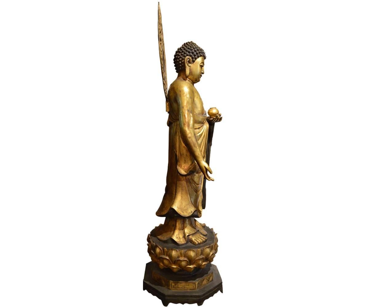 This is just a spectacular, large gilt bronze Buddha with a headdress or halo that contains an incredible amount of detail. Buddha is standing on a lotus flower that rests on a stand with legs raising the piece above the ground.

On the chest of