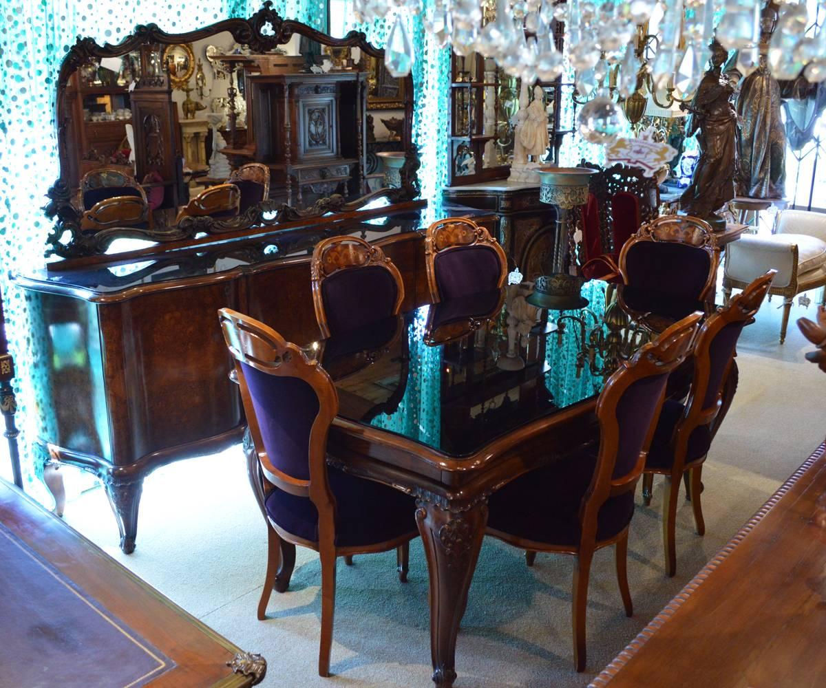 This 1930s Italian walnut dining set features six inlaid marquetry chairs with newly re-upholstered dark royal purple velvet fabric and a black glass table. The set is entirely hand carved and the sideboard feature walnut burl wood. The sideboard