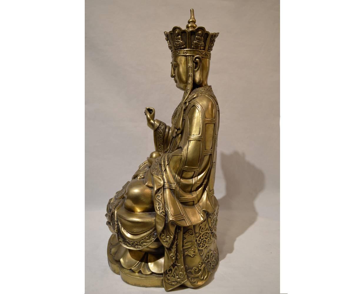 This gilt bronze Quan Yin holding a small sphere is seated upon a double lotus flower and has elaborately detailed flowing robes and headdress. There are Chinese characters at eh base of the statue.