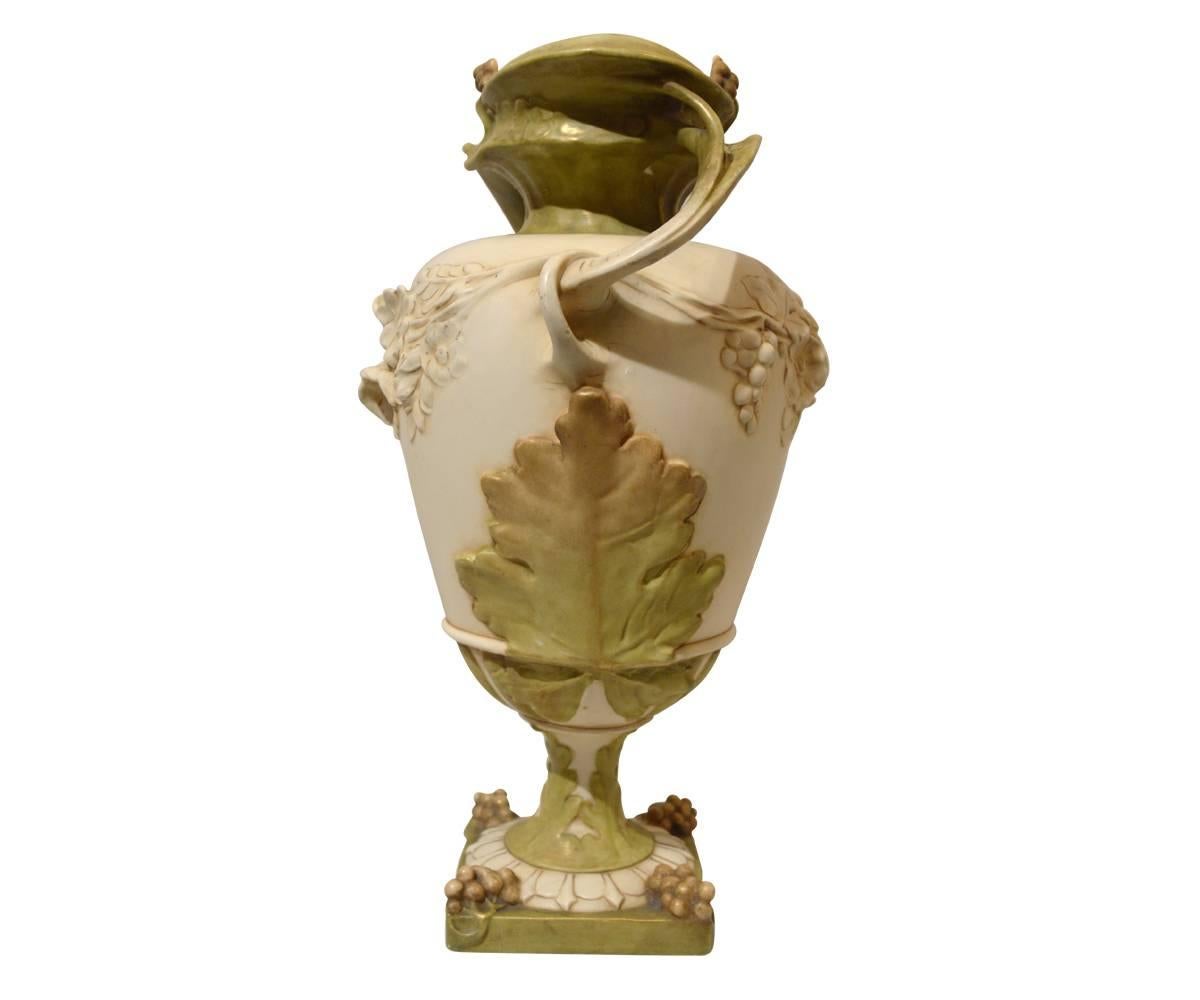 This pair of Royal Dux vases are decorated with grapes and floral vines. The vases are marked on the bottom as shown. An ivory color with soft green accents make up the palate. Swerving handles on both sides connect to rings in these Art Nouveau