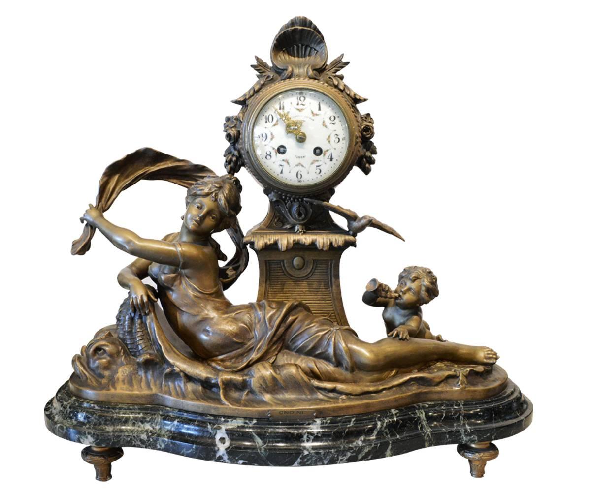 This antique clock and urn garniture is of French origin and in the Louis XVI style. The clock features a female and baby in an ocean setting with birds and shells. The Urns have a flame on the top and three ram heads with a coat of arms and garland
