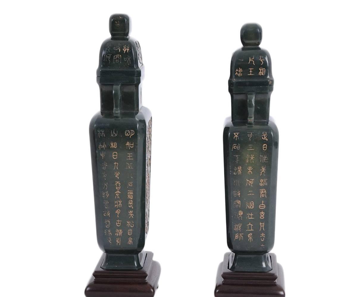 This is a pair of Chinese carved spinach jade covered urns; each with a faceted and tapered form. The panels contain a gilt dragon to the front and verso and also contain gilt incised Archaistic calligraphy to the sides. The handles are scrolled