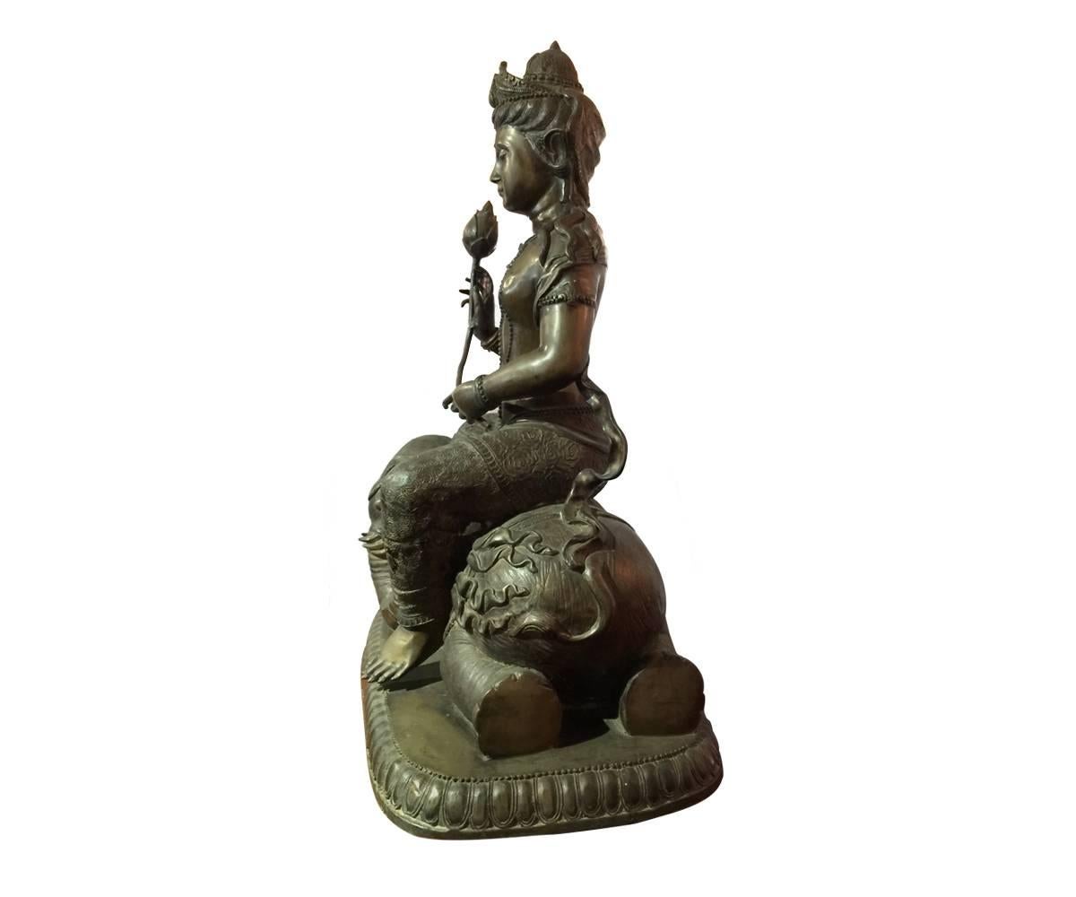 This is a large bronze Quan Yin seated on an elephant and holding a flower. The piece definitely has age to it but we are unable to confirm its precise age and therefore will leave further research up to the new owner. This is a great size and she