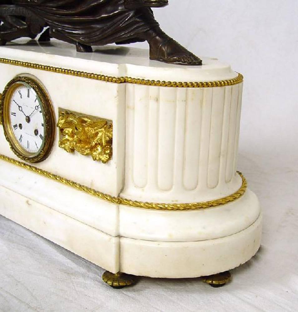This rare French set features a bronze clock with statue and two matching candelabras. The bases are a luxurious creamy white marble in a Doric column motif. Each marble piece is offset by gilt bronze decoration. Around the base is a golden twisted