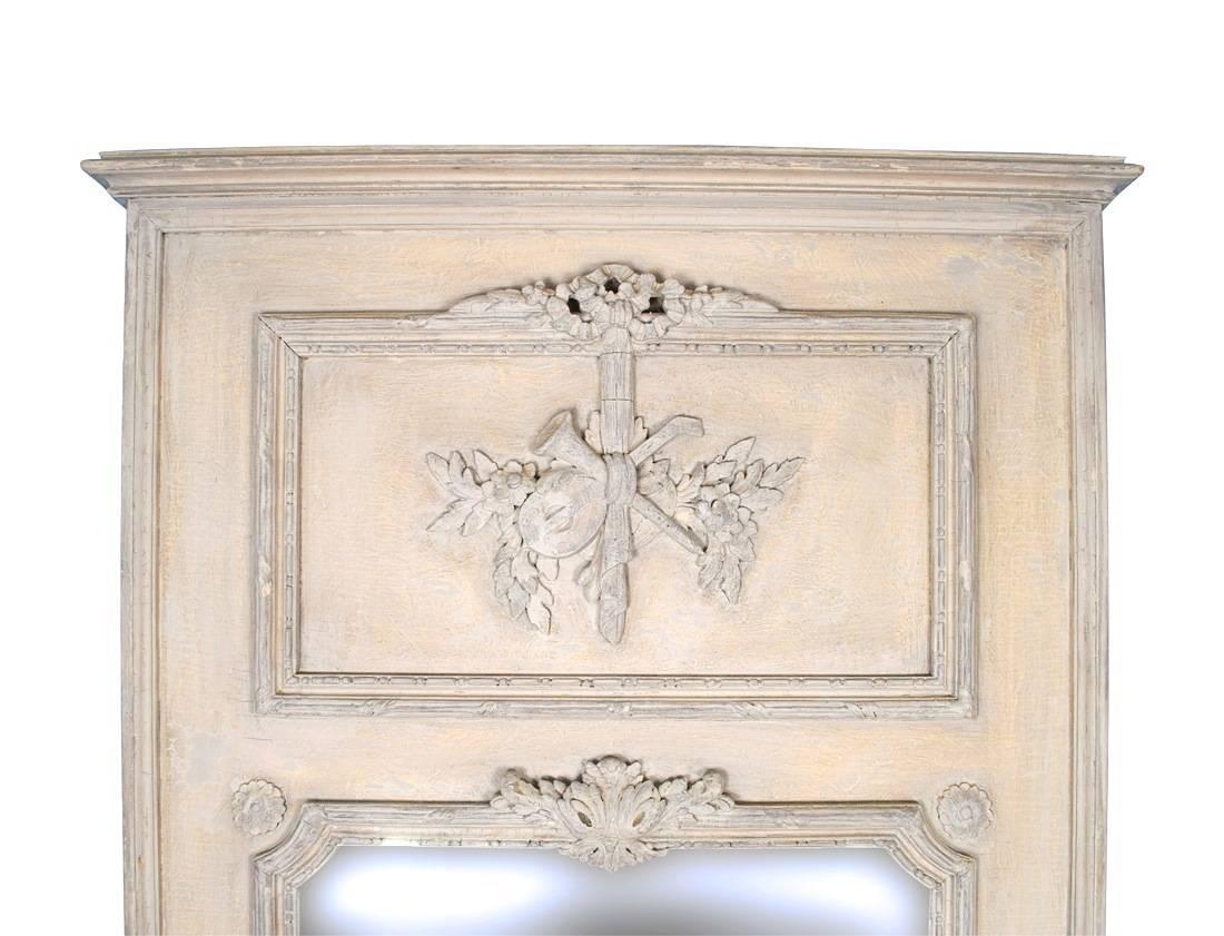 A striking pair of wooden trumeau mirrors with elegantly carved decoration and distressed paint. Each mirror is decorated with a vignette with musical and floral relief carvings in neoclassical style. Acanthus leaf and two medallions embellish the