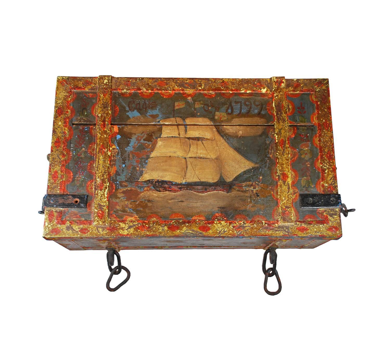 An antique wooden steamer trunk elaborately painted and well aged. The wood is painted with a base of blue and then decorated with white, yellows, greens and reds. Painted on the lid is a sail boat and -Cadiz a 1799-. The front bears painted flowers