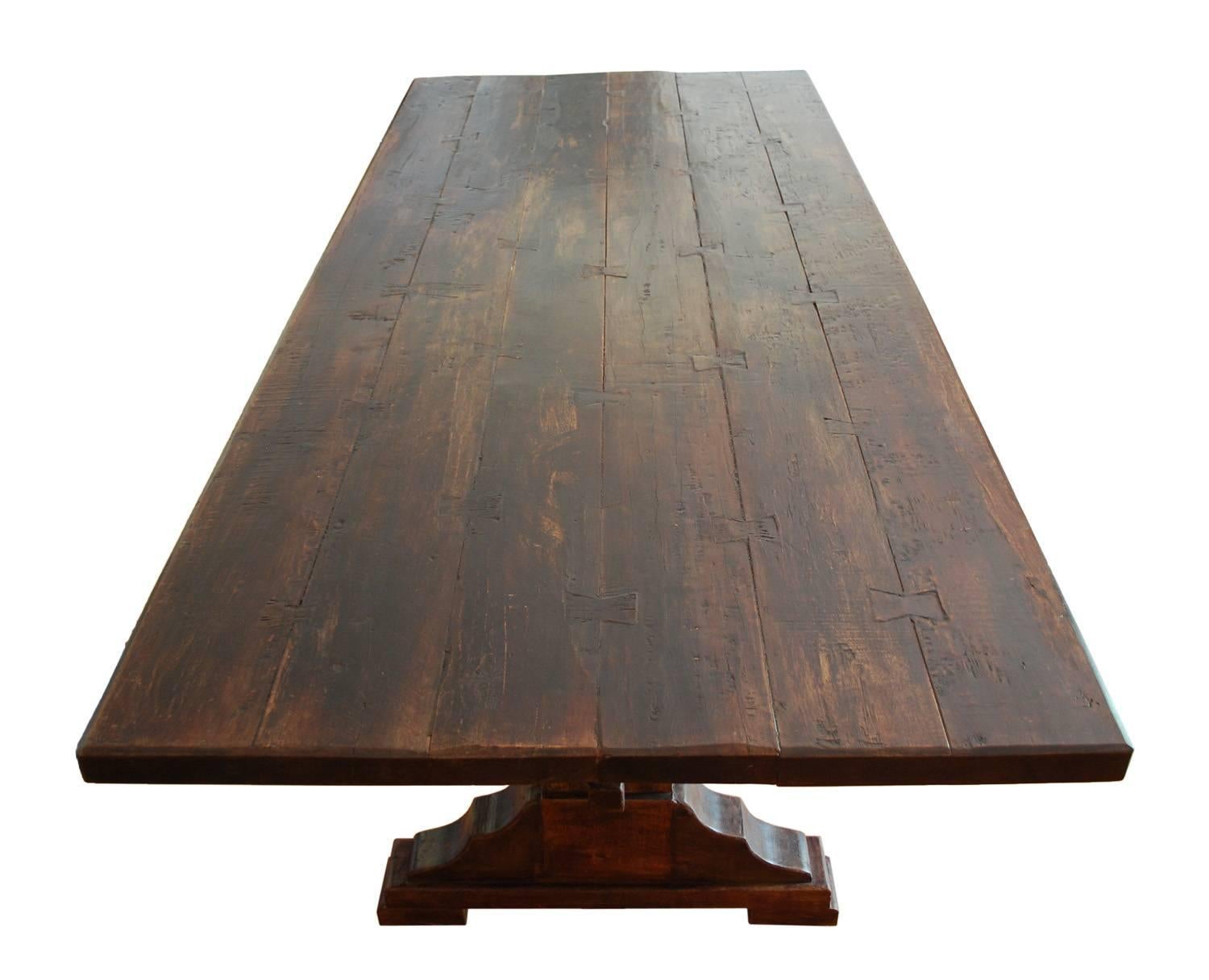 An impressive solid wood teak trestle table with rustic construction in antique style. Five hewn planks are connected with butterfly joints to make the tabletop. Two sturdy legs with broadly scalloped supports are joined by a straight post stretcher