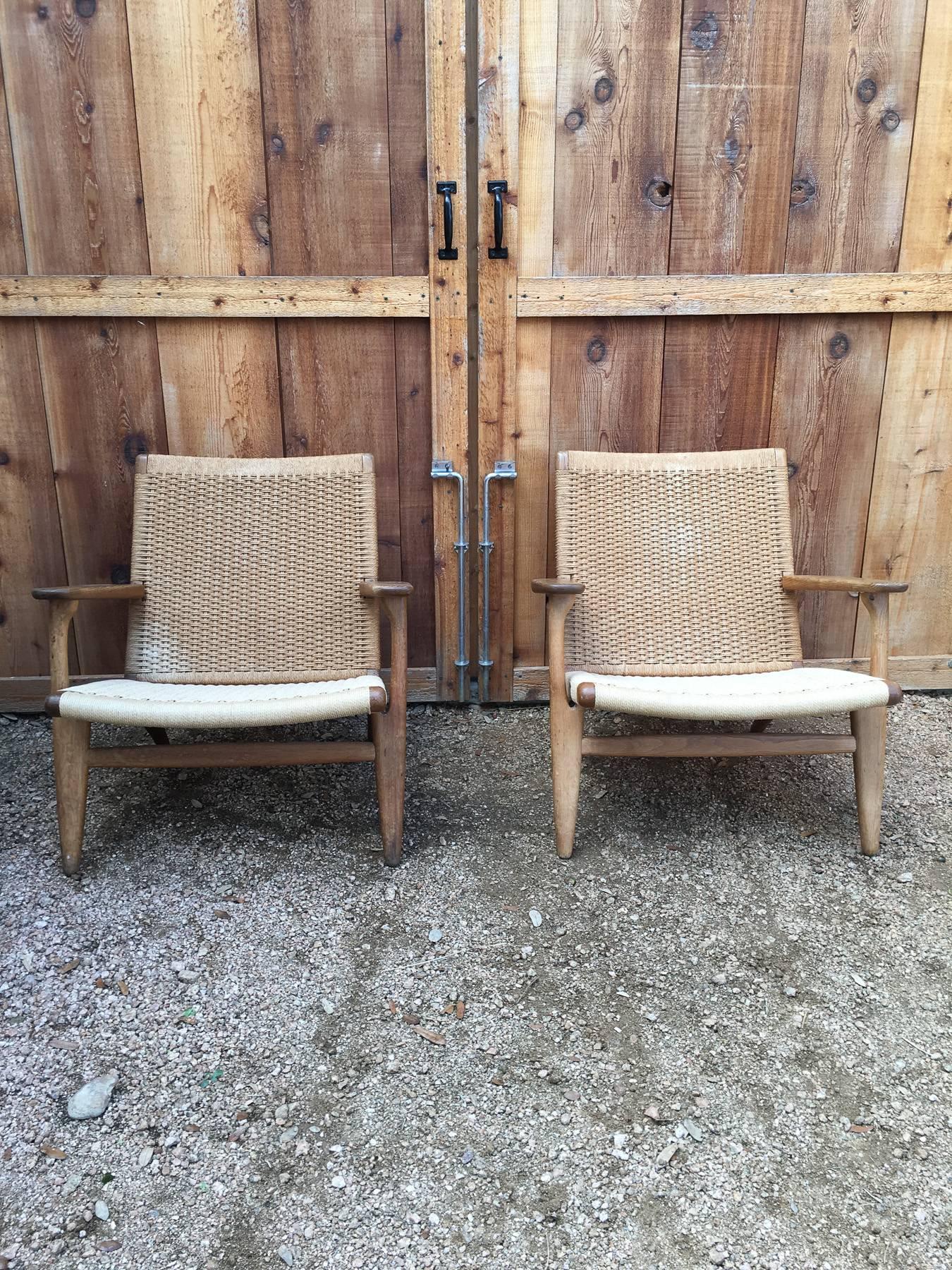 Pair of vintage Hans Wegner CH25 lounge chairs. Woven paperboard seats on a solid oak frame.