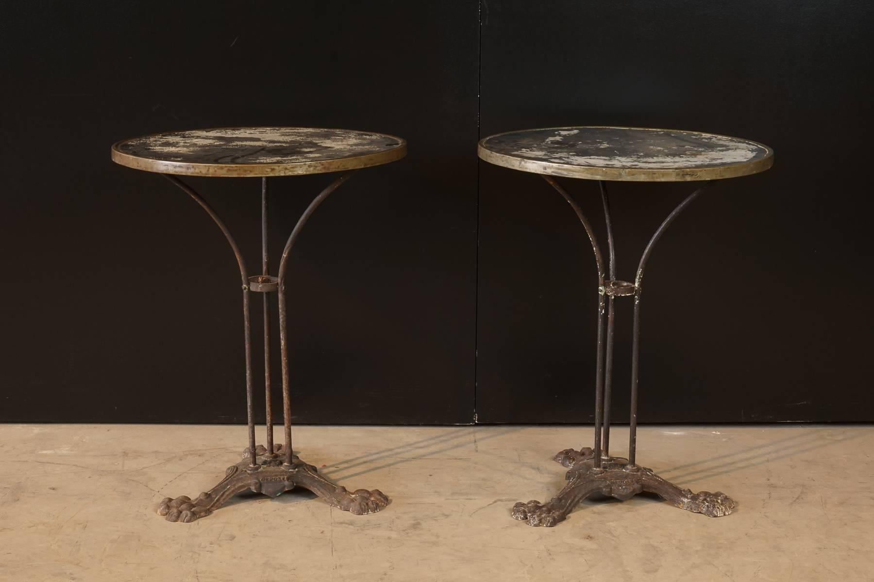 Pair of French Bistro Tables, circa 1930. Iron base with claw foot detail and marked "Depose." Metal top with brass edge.