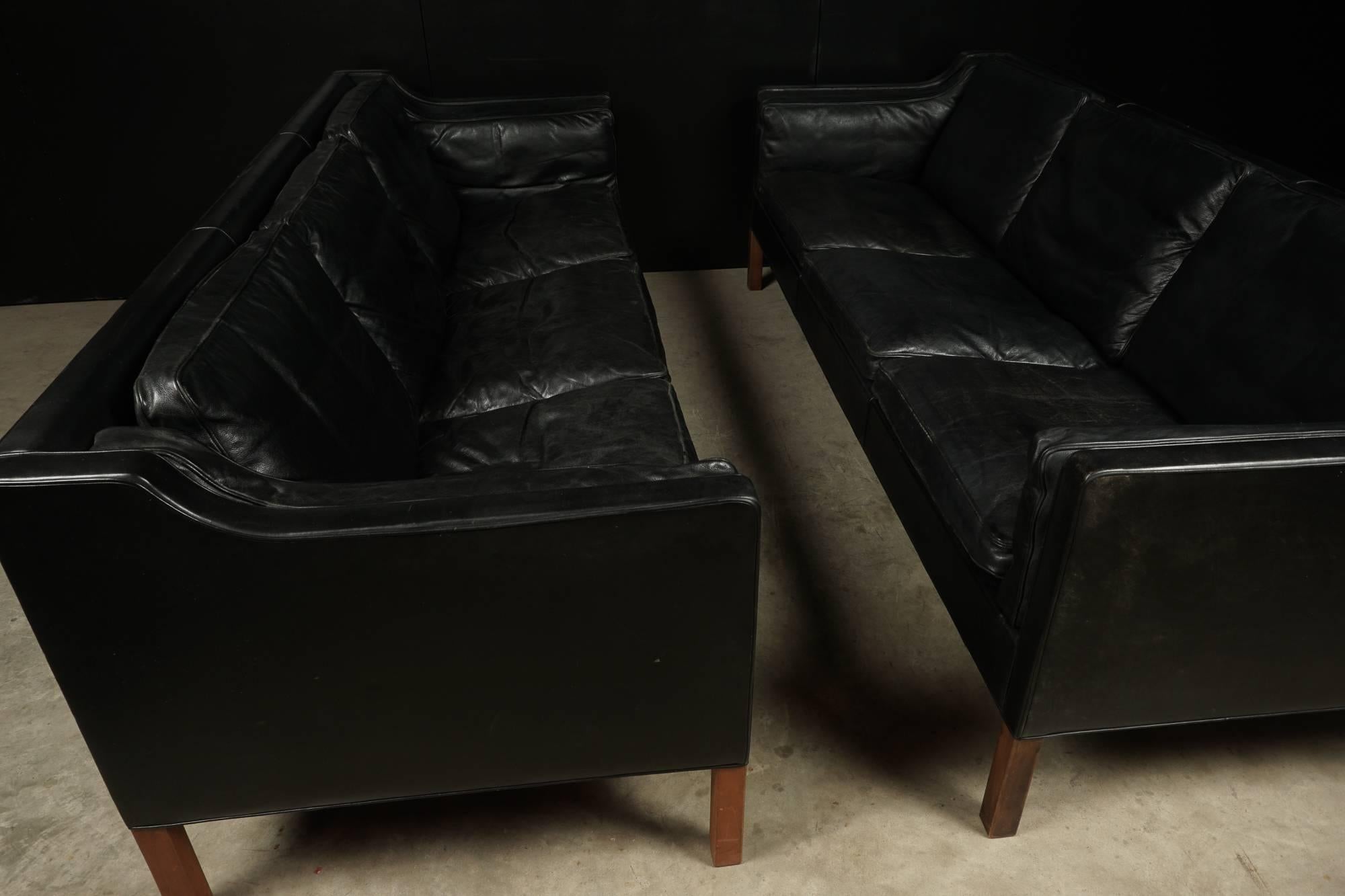 Pair of Børge Mogensen three-seat sofas, model 2213 by Fredericia Stolefabrik, Denmark. Down filled cushions covered in black leather with solid teak legs.