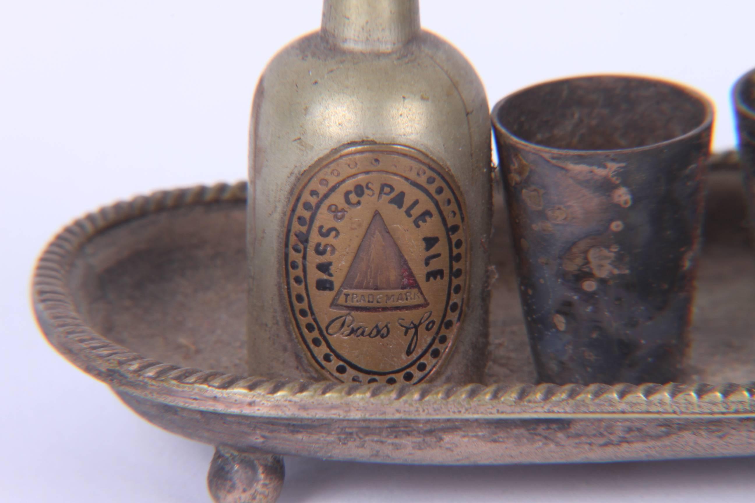 A wonderful and rarely seen cast metal advertising miniature with two bottles and drinking cups on a tray. Both Guiness Extra Stout and Bass Pale Ale are represented. Age appropriate wear and age patina.