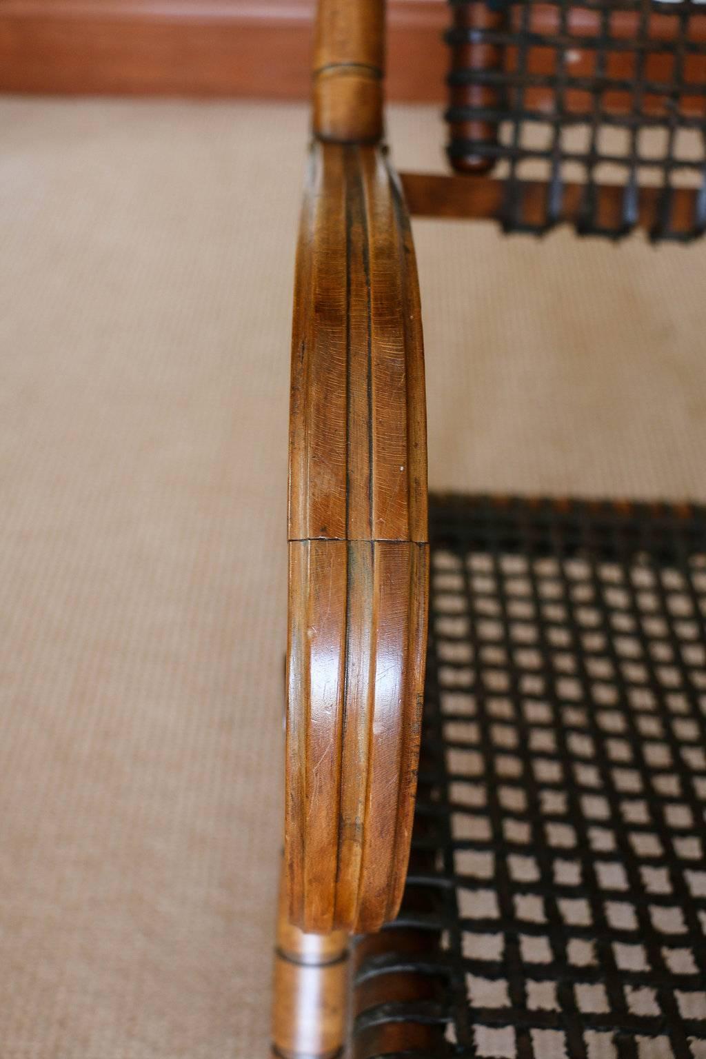 Fine form with one broken strap and geometric moulding at upper right missing. The back with the wire webbing flanked by bamboo form frame, and bold swirled arms with inverted trumpet finials. Stamped, 