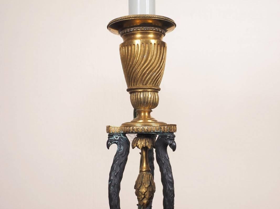 Pair of candlestick lamps with bronze fluted bobeche with patinated figural supports on a conforming fluted brass base with inverted leaf form final raised on a marble and beaded plinth base. The lamps with ebonized and gilt tole shades and an arrow