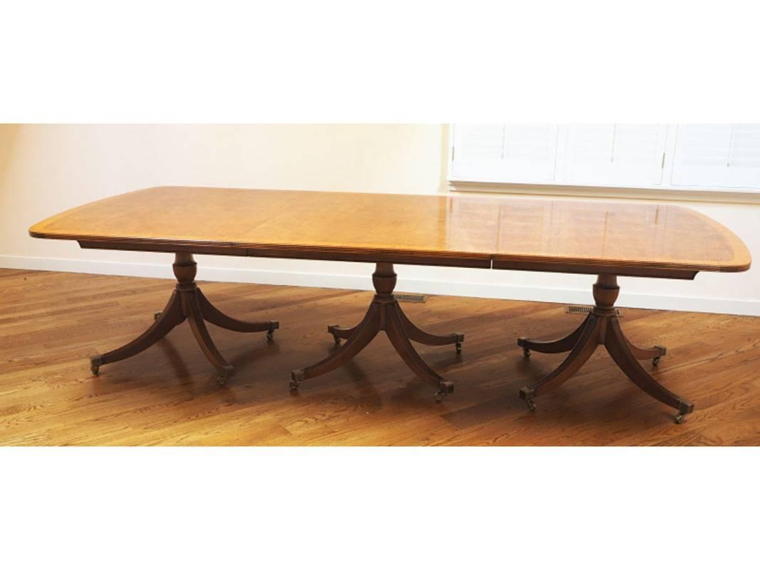 An impressive triple pedestal dining room table with four leaves and storage racks. The table still bearing the Smith and Watson paper label. The table with cross banded top, urn form column with fluted legs, brass caps all raised on brass casters.