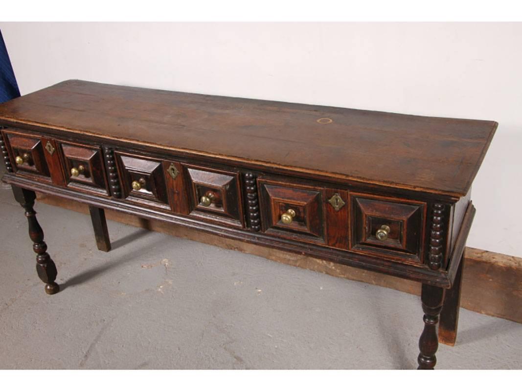 First quarter of the 18th century. Dark stained oak with a good patina. Carved drawers with bobbinn half turned columns, raised on a block and baluster turned legs.
Condition: Round water stain to top, old ink stains that add to the character. Age