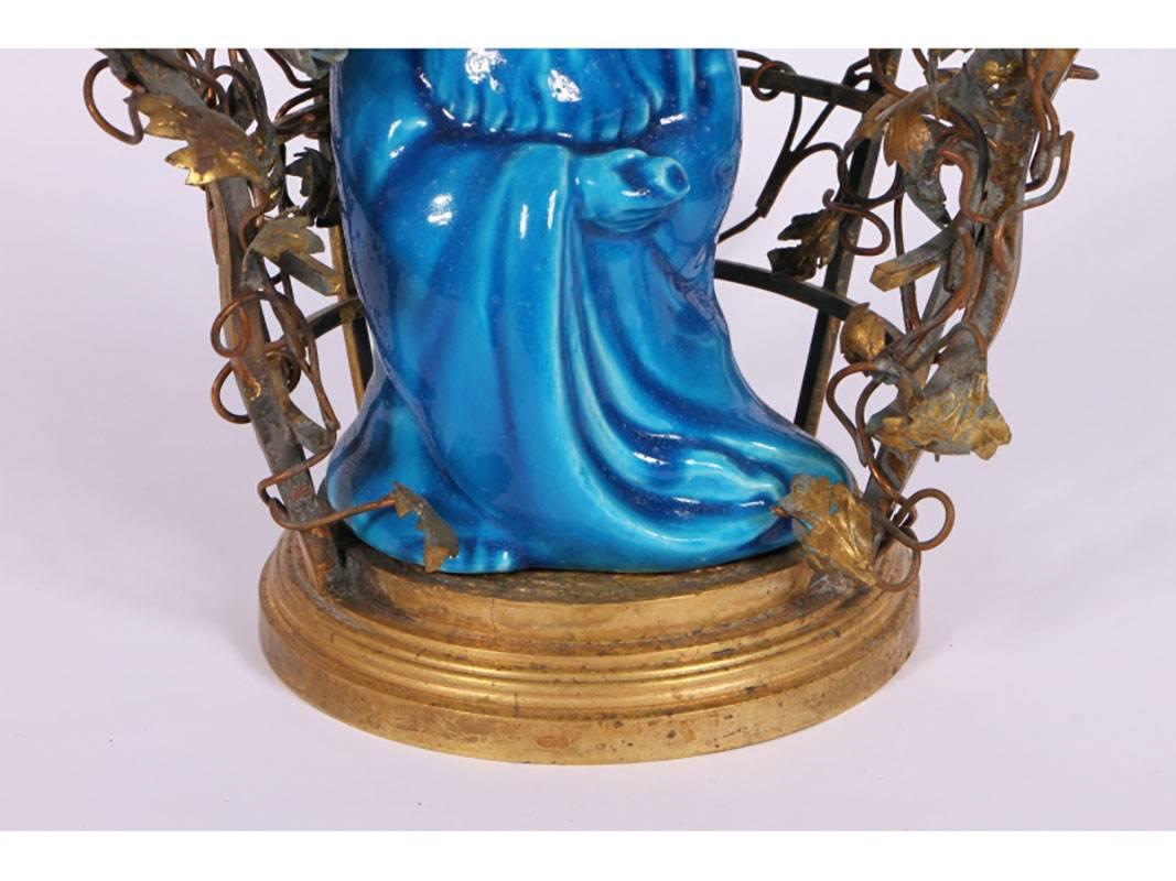 Turquoise glazed ceramic Buddha figure surrounded by iron worked lattice and foliate garden with two candleholders light fixtures.
Condition: Small flower with chip, needs to be rewired.