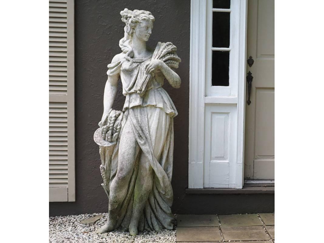 Two life-sized female neoclassical garden figures, one holding sheaves of wheat, the other flowers, raised on plinth bases.
Condition: Consistent with age and weathering.