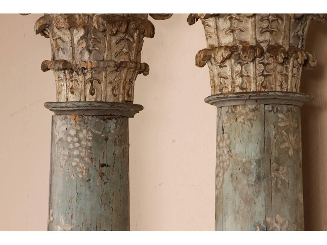 A wonderful pair of solid wood corinthian columns in three parts. Columns in celestial blue having hand-painted grapes and vines. The capitals heavily carved with acanthus leaves. The bases are gesso with a spiral acanthus leaf floral. Columns are