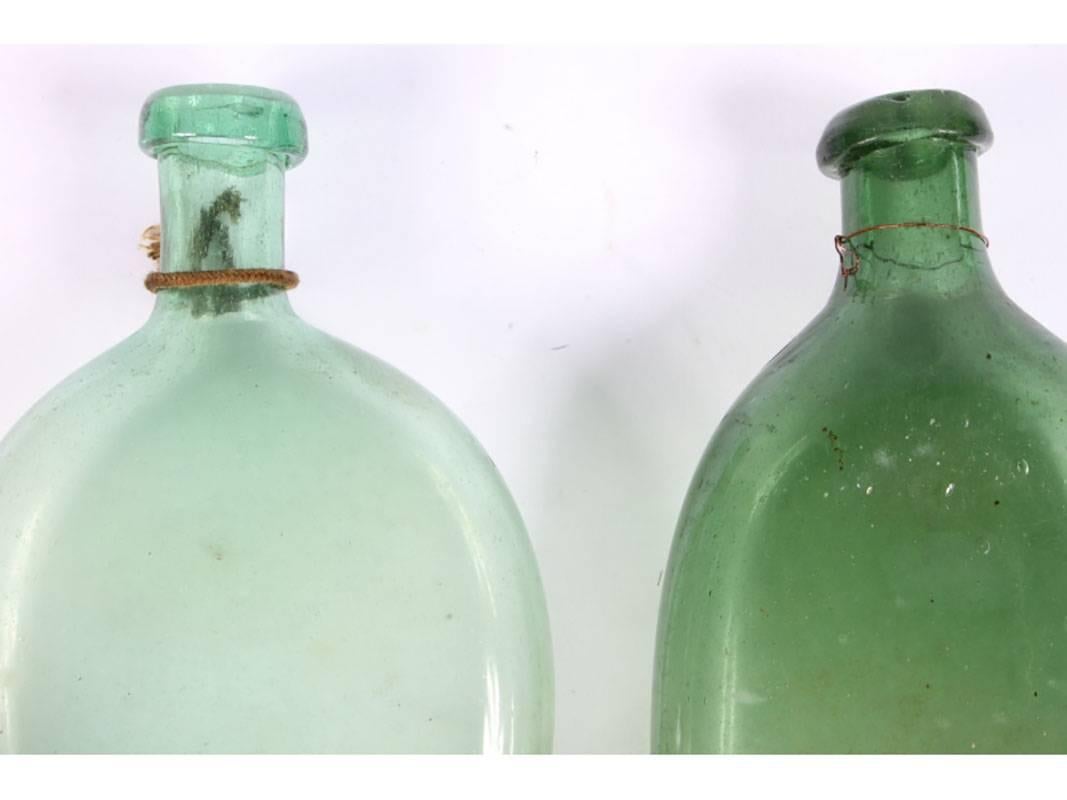 A collection of Spanish glass in the shape of flattened flasks, ranging in color from greenish brown, aqua and forest green. The smallest measures: 2