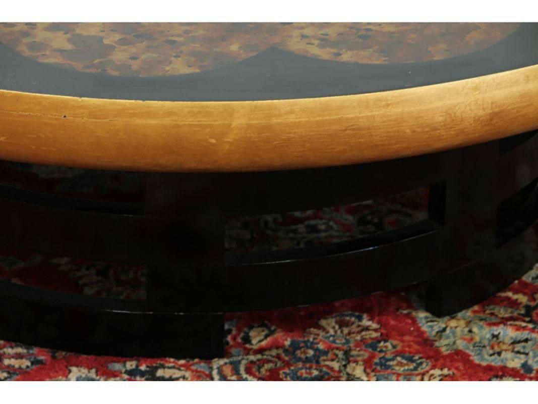 A Kittinger coffee table by Herman Muller and Isabel Barringer. The Mid-Century inspired design featuring a round top with faux tortoise shell gold leaf motif. Condition: Craquelure to top and a small loss about the size of a nickel to black border