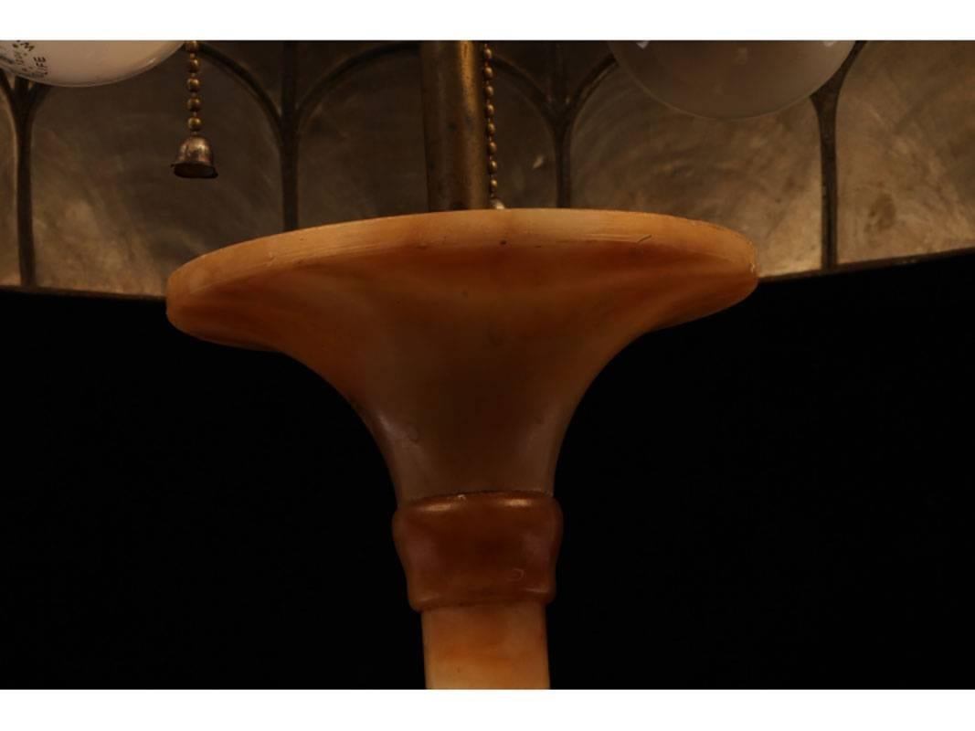 Carved marble lamp depicting a bird feeding her babies on a faux nest mounted on a plinth base. The lamp has a trumpet form column and is crowned with a magnificent capiz shell dome shade with an acorn finial. Significant details including carved